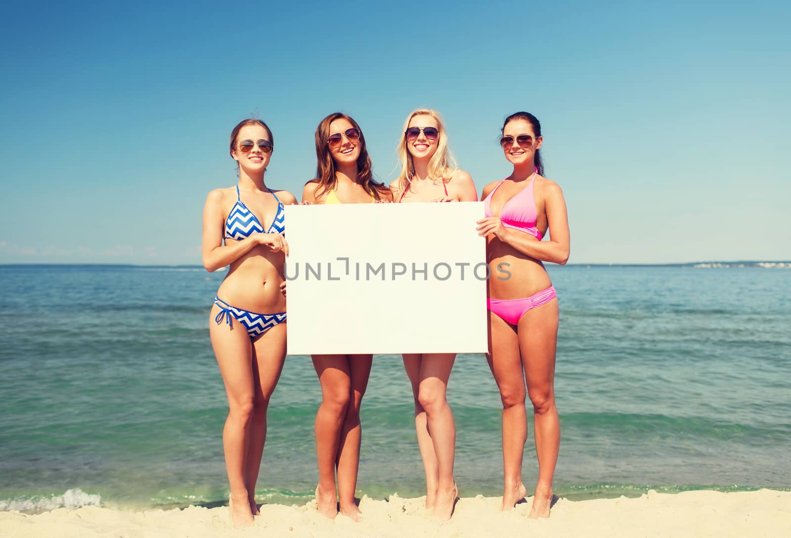 summer vacation, holidays, travel, advertising and people concept - group of smiling young women with big white blank billboard on beach