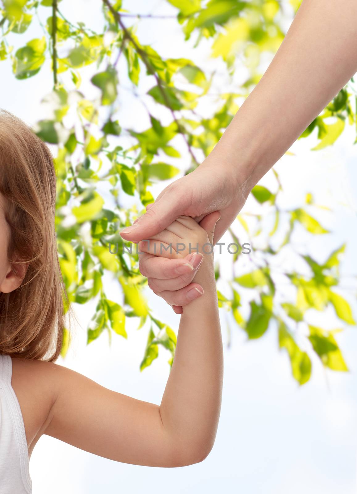 people, charity, family and adoption concept - close up of woman and little girl holding hands over green tree leavers background