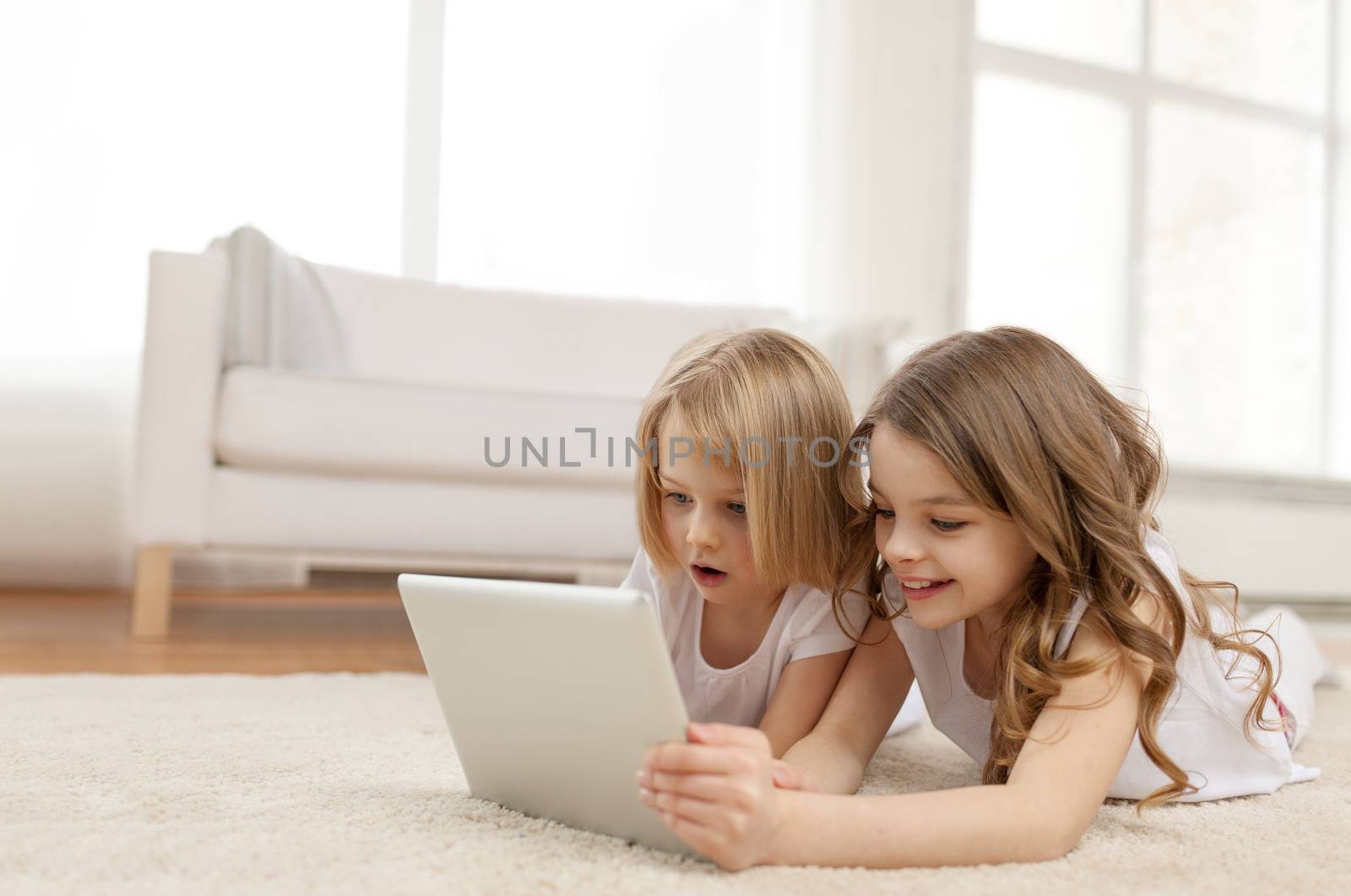 children, technology and home concept - two little girls with tablet pc computer lying on floor at home