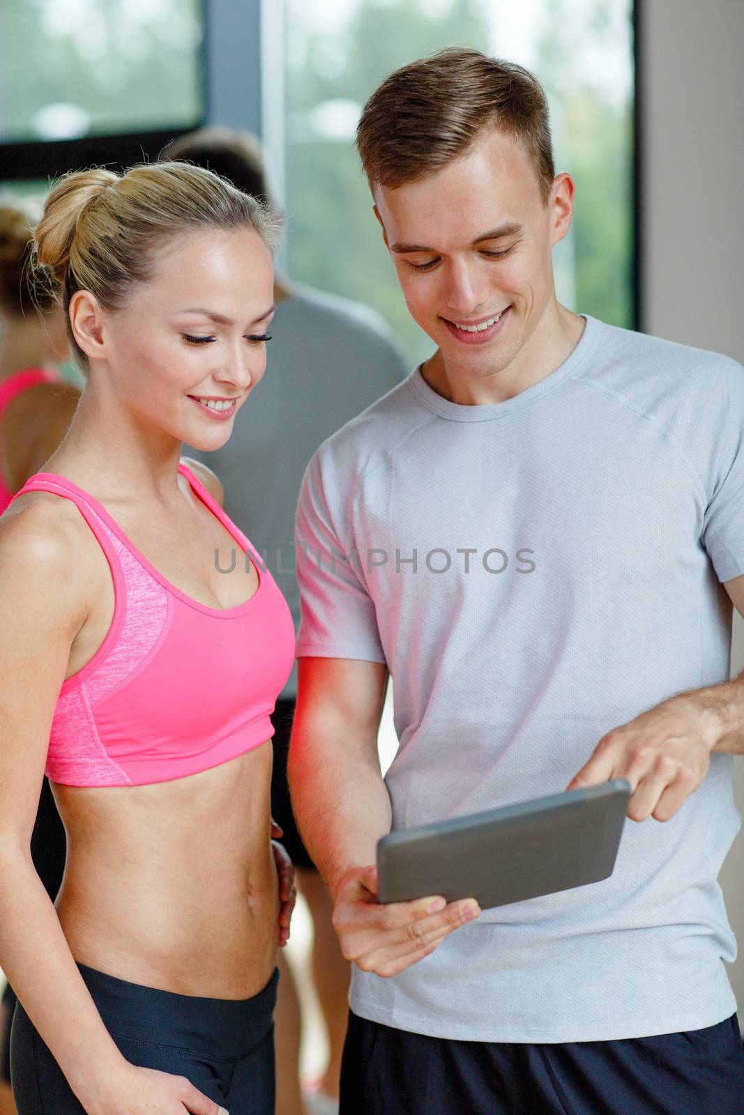 smiling young woman with personal trainer in gym by dolgachov