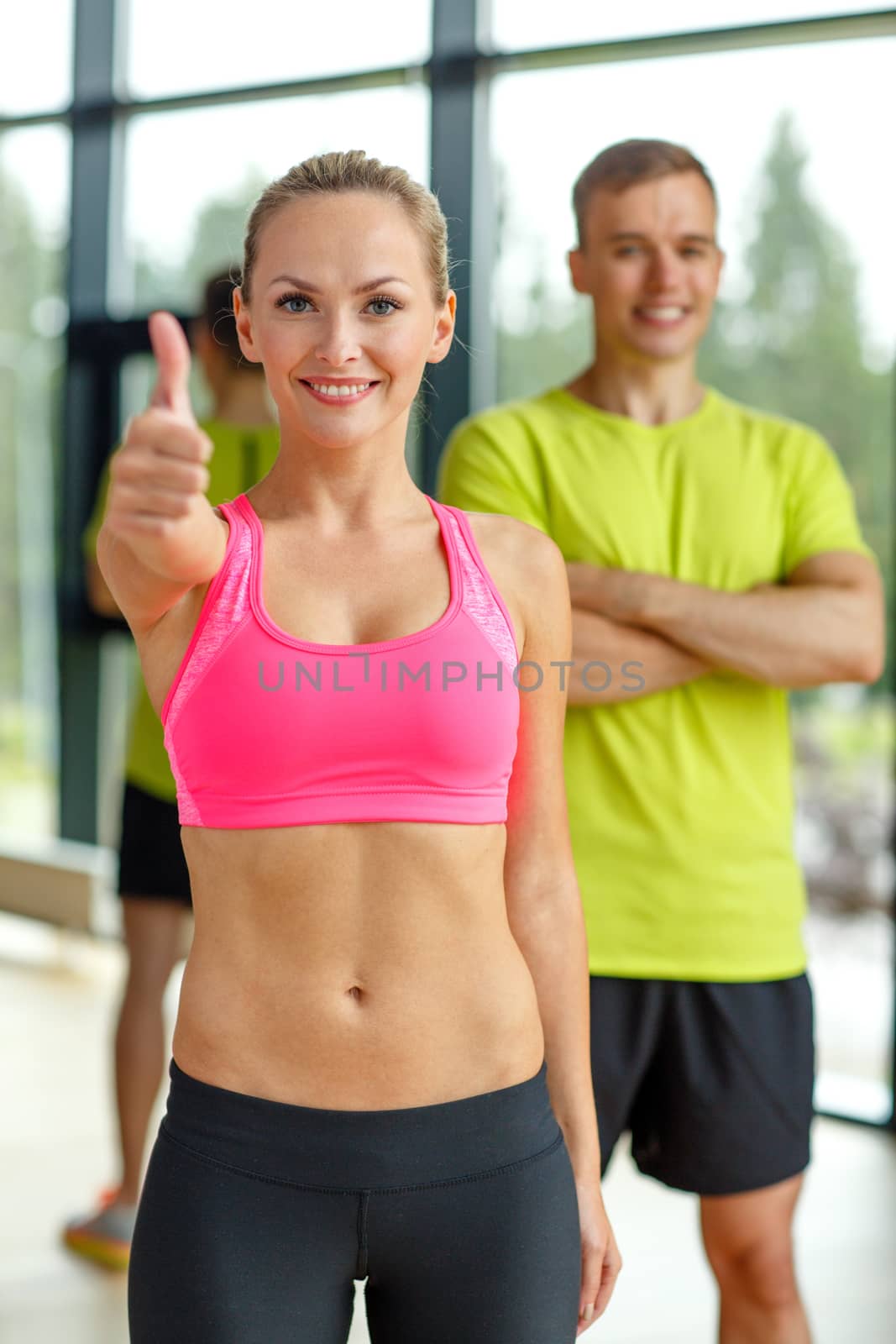 smiling man and woman showing thumbs up in gym by dolgachov
