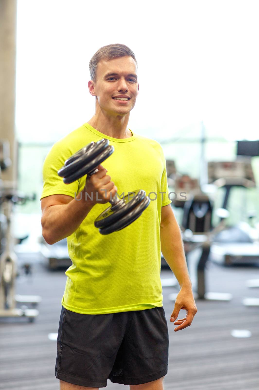 smiling man with dumbbell in gym by dolgachov