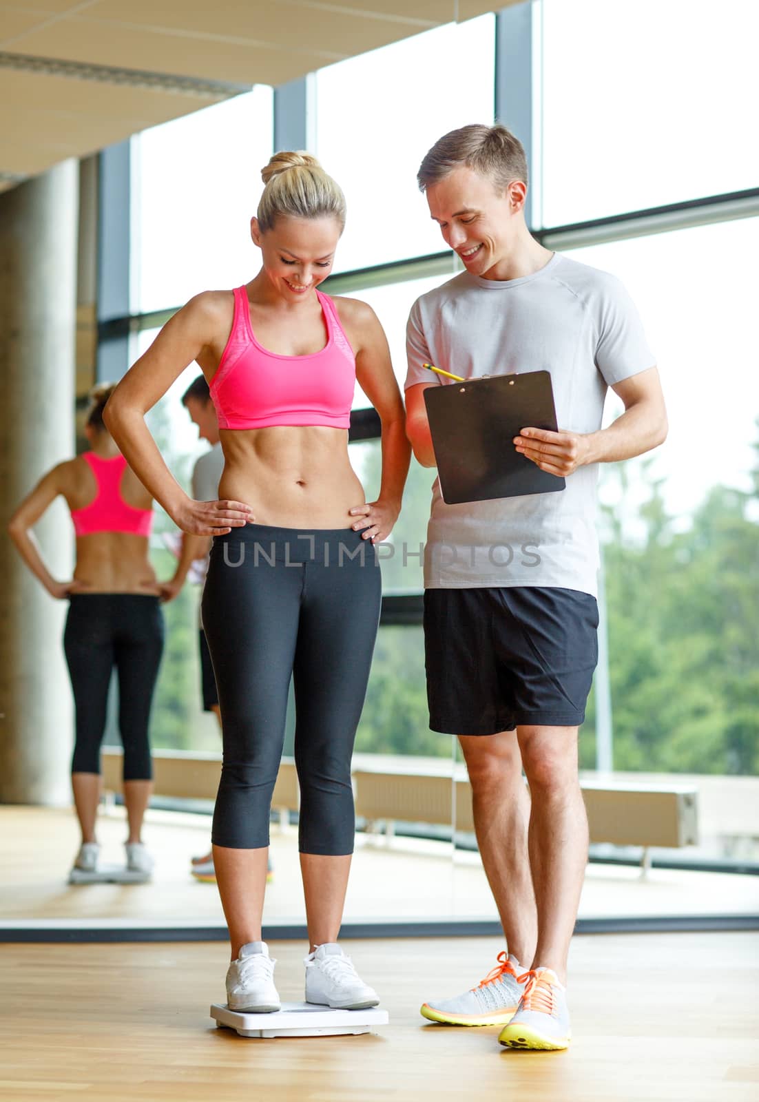 sport, fitness, lifestyle and people concept - smiling man and woman with scales and clipboard in gym