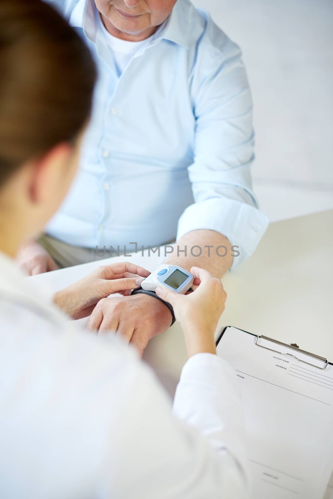 healthcare, oldness, cardiology and medicine concept - close up of doctor measuring pulse or blood pressure with wrist tonometer to senior man in hospital