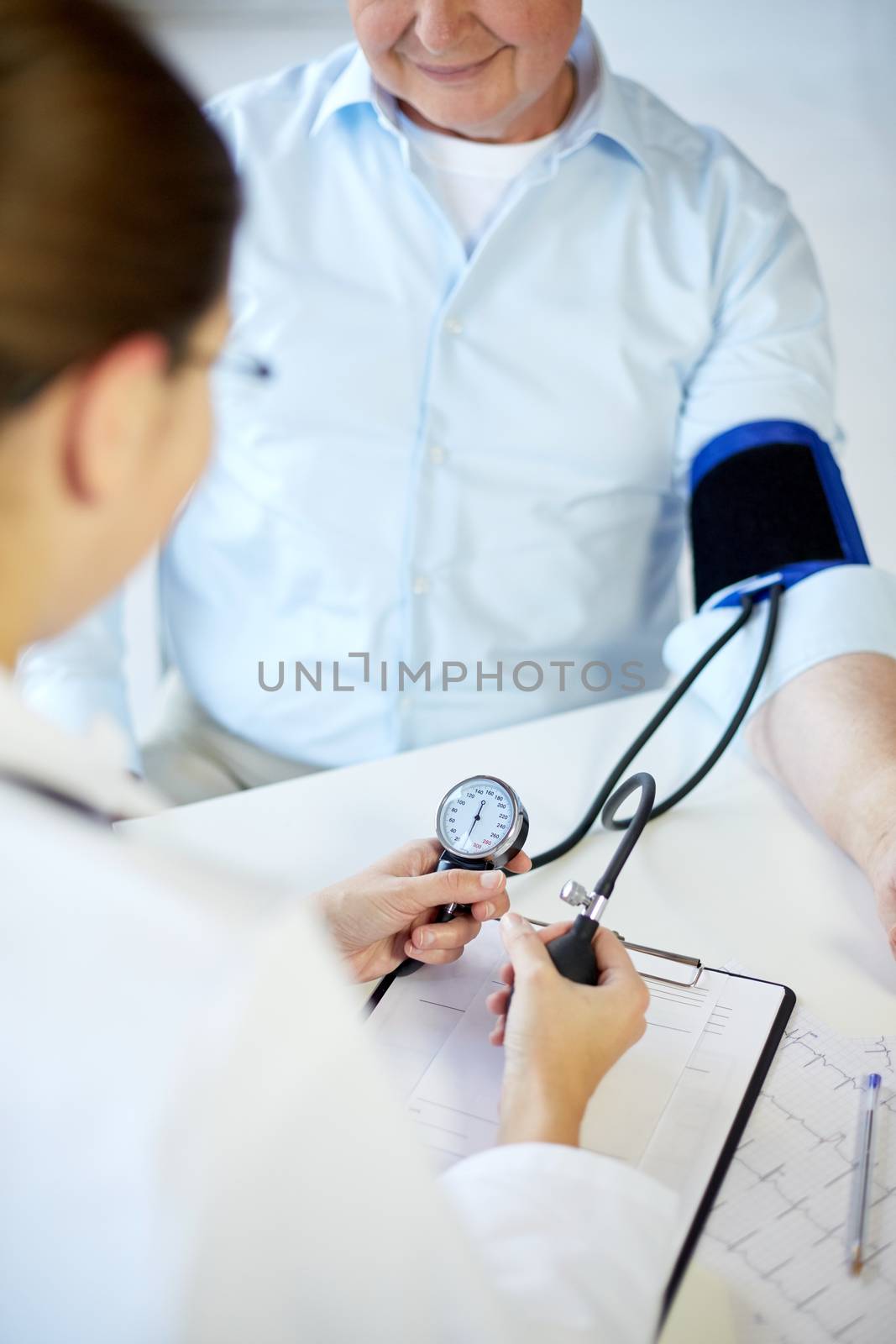 healthcare, elderly and medical concept - close up of female doctor or nurse measuring blood pressure to senior male patient with tonometer in hospital