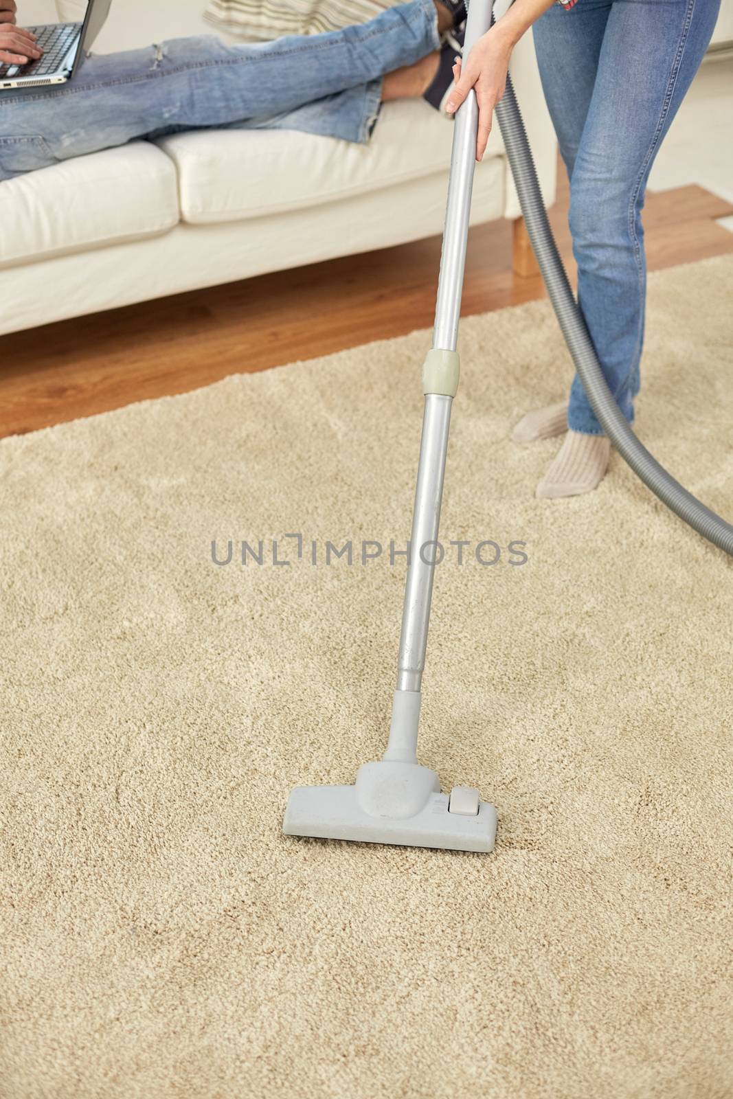 people, housework and housekeeping concept - close up of couple legs and vacuum cleaner on carpet at home