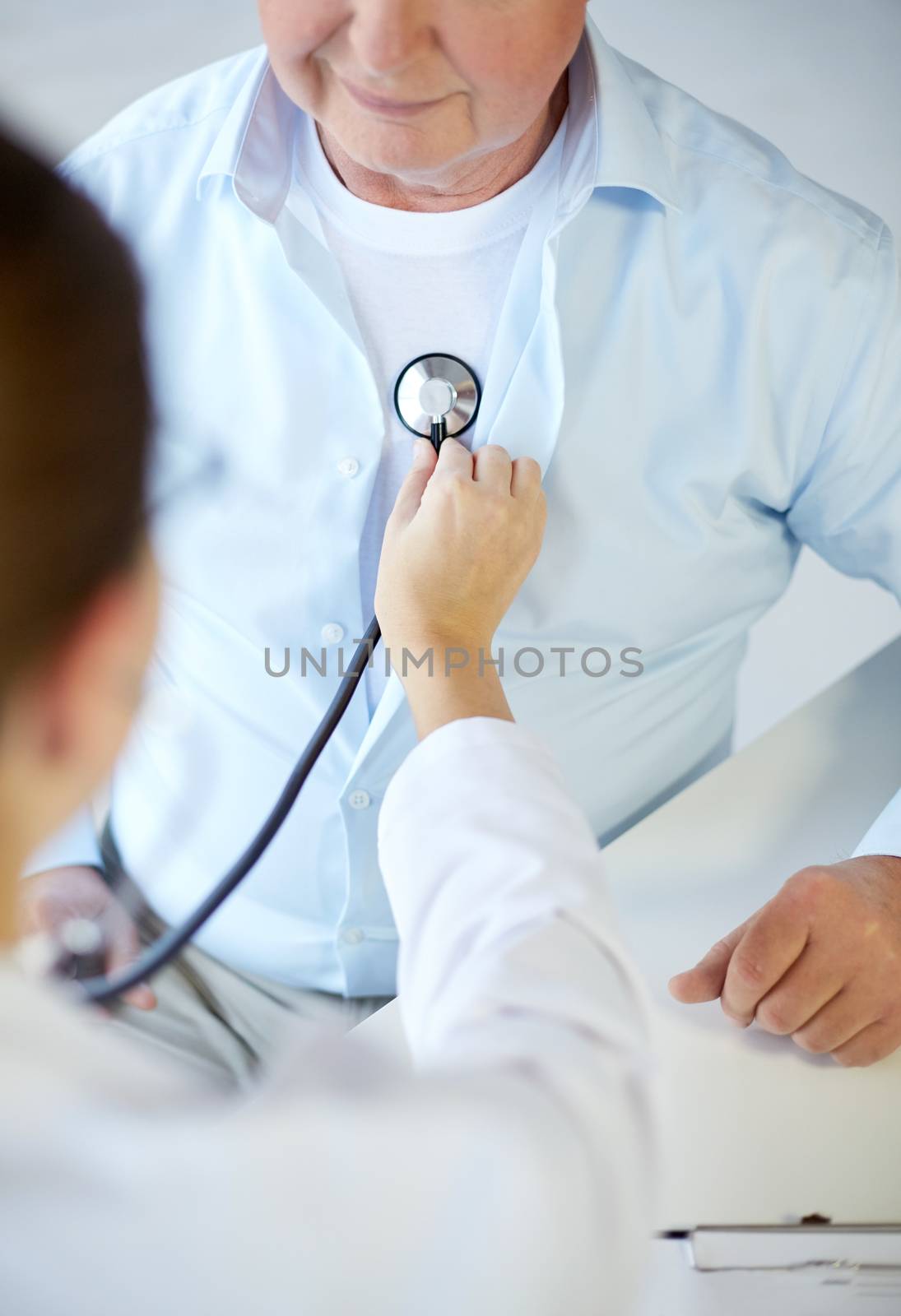 healthcare, elderly and medical concept - close up of doctor with stethoscope listening to senior man breath or heartbeat in hospital