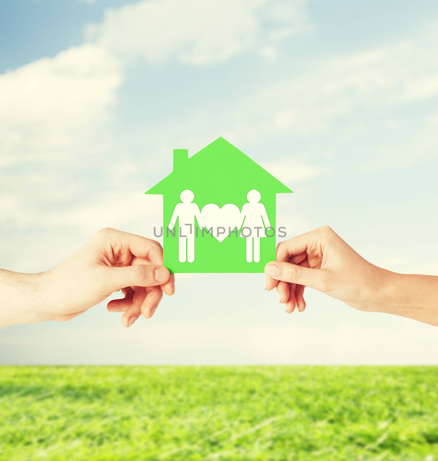 real estate and family home concept - isolated picture of male and female hands holding green paper house with family