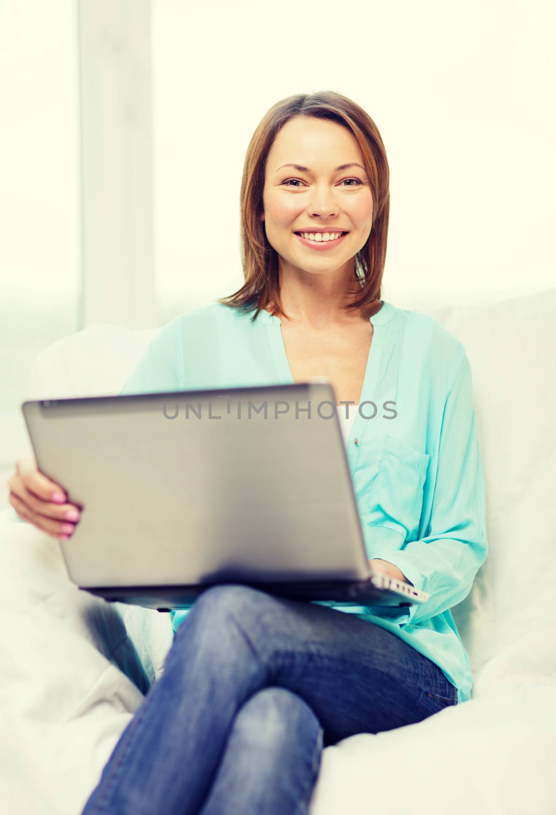 home, technology and internet concept - smiling woman sitting on the couch with laptop computer at home