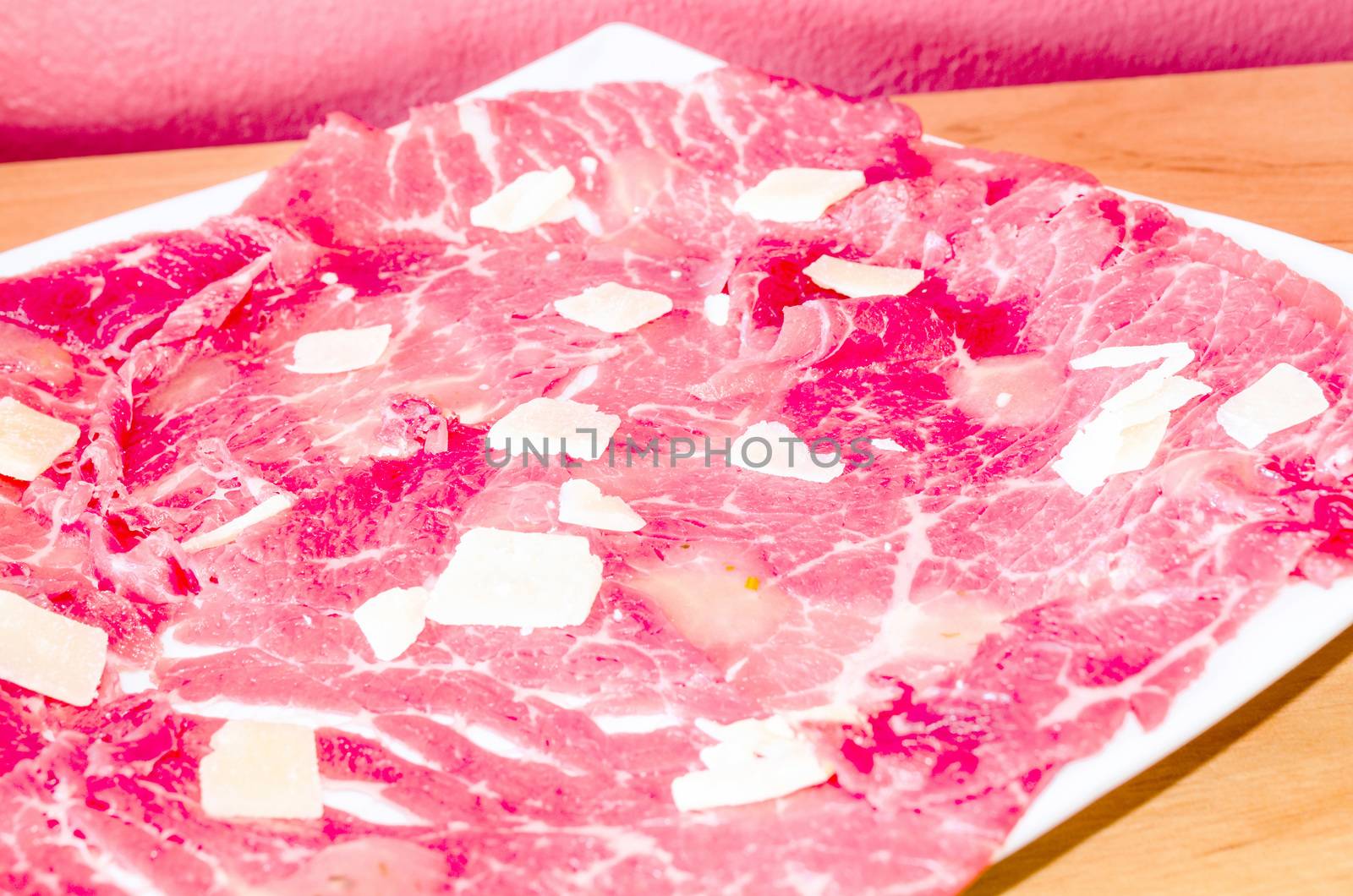 White dish with carpaccio of beef with parmesan.