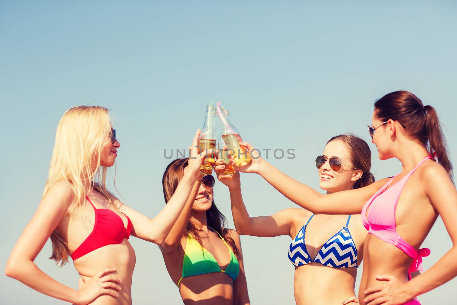group of smiling young women drinking on beach by dolgachov
