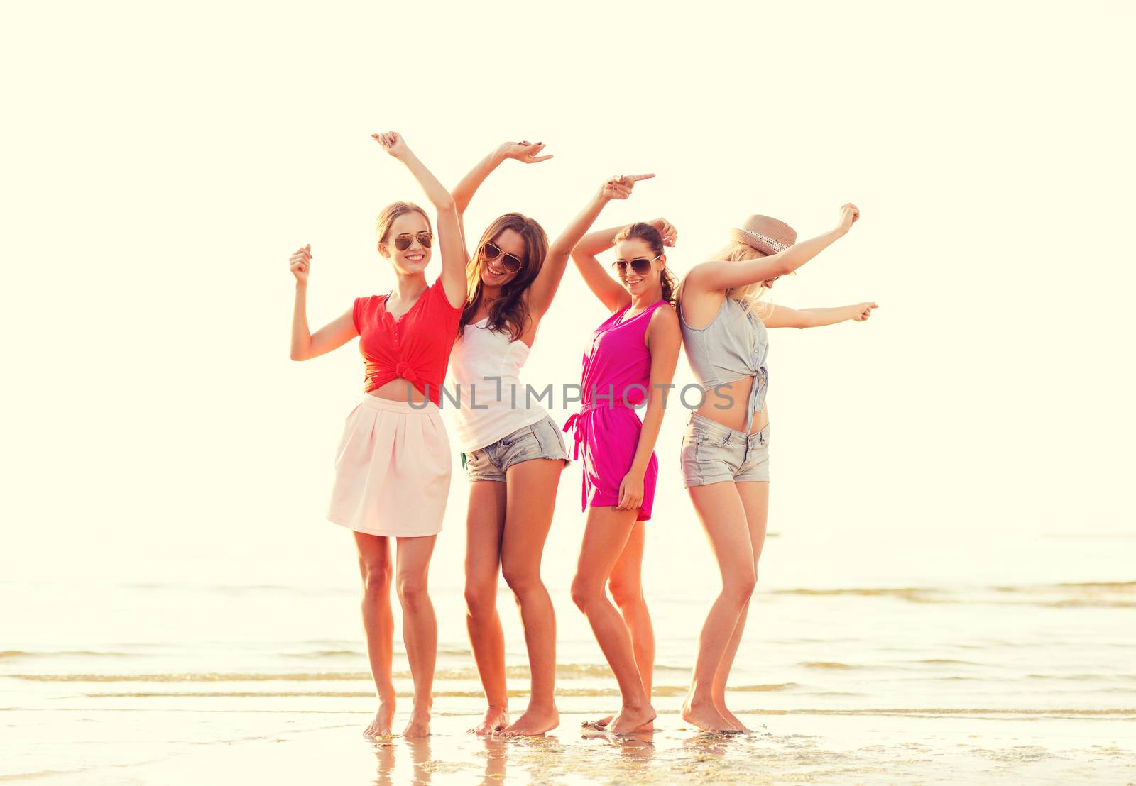 summer vacation, holidays, travel and people concept - group of smiling young women in sunglasses and casual clothes dancing on beach