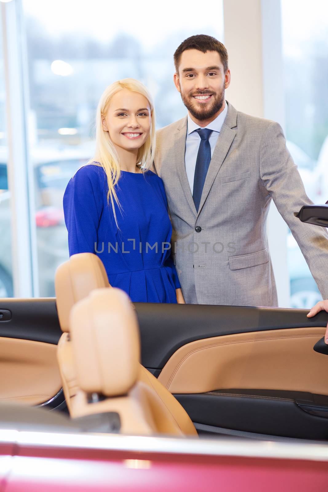 happy couple buying car in auto show or salon by dolgachov