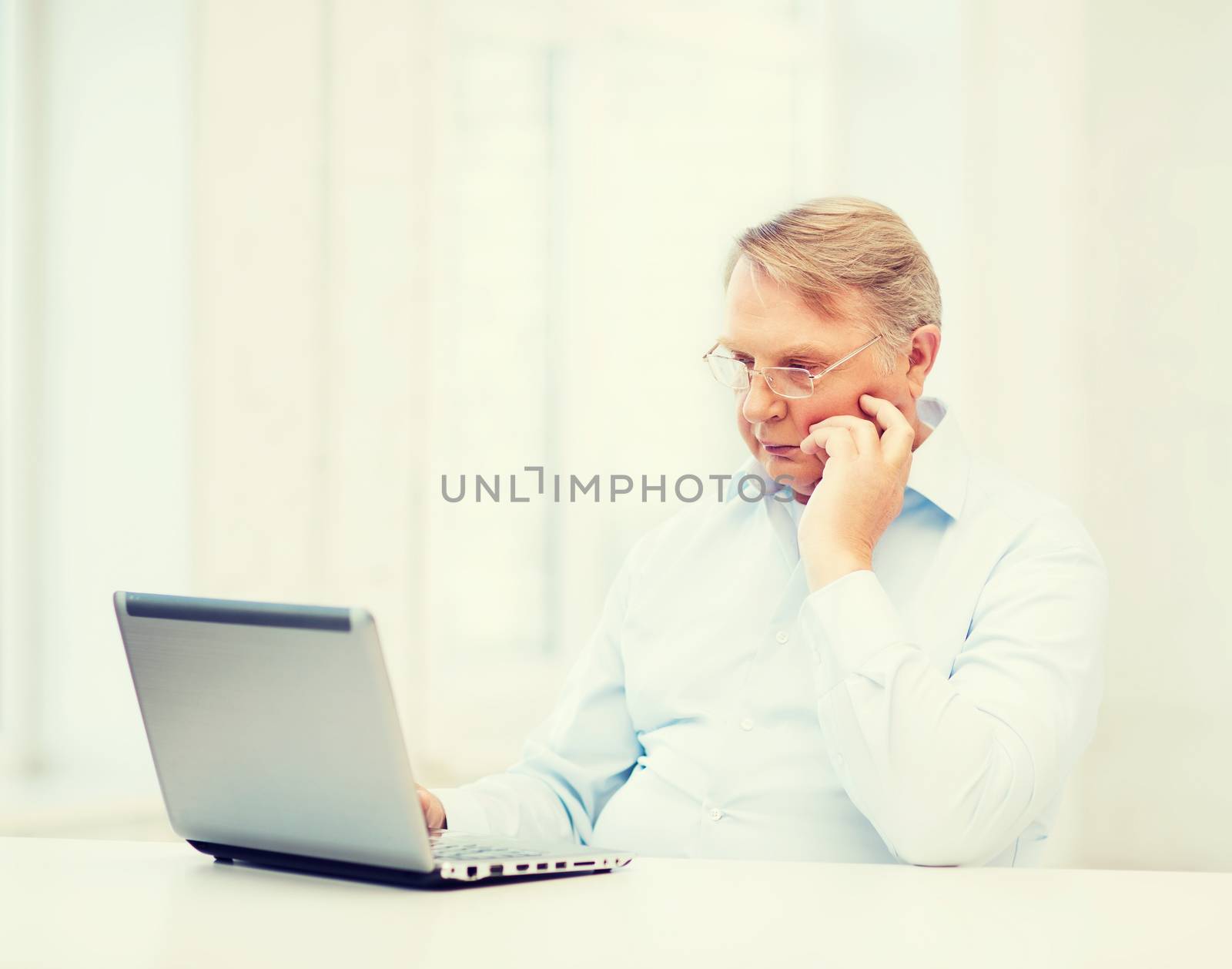 technology, oldness and lifestyle concept - old man in eyeglasses working with laptop computer at home