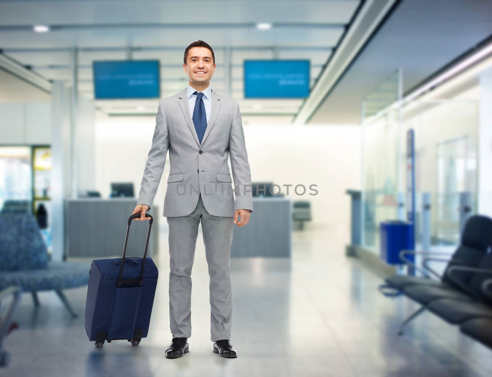 business trip, traveling, luggage and people concept - happy businessman in suit with travel bag over airport background