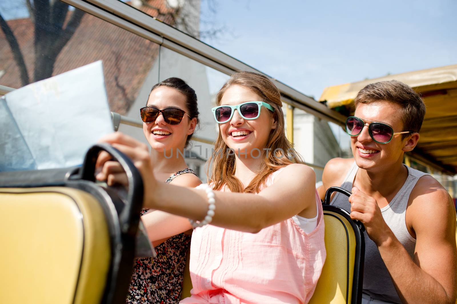 friendship, travel, vacation, summer and people concept - group of smiling friends with map traveling by tour bus