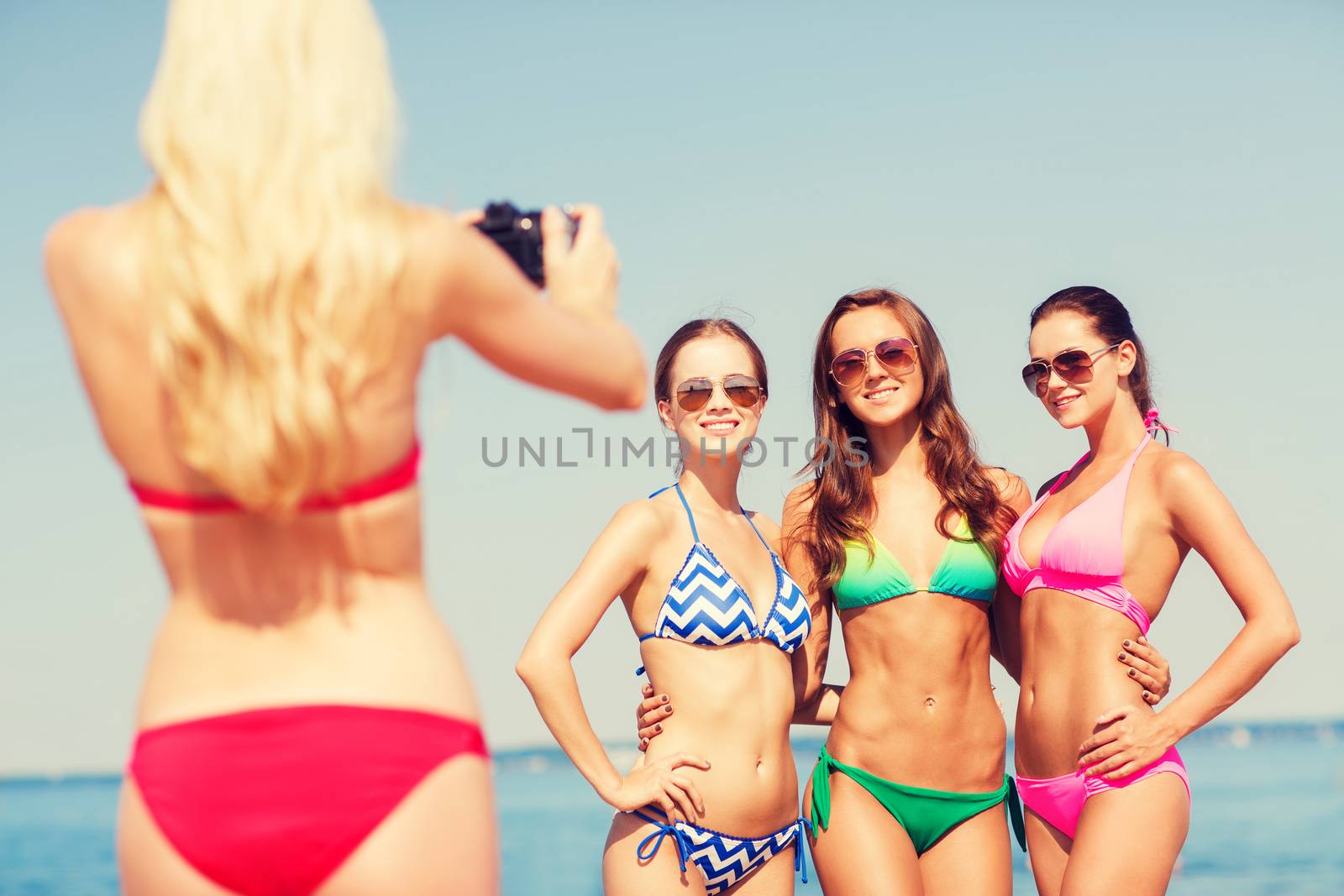 group of smiling women photographing on beach by dolgachov