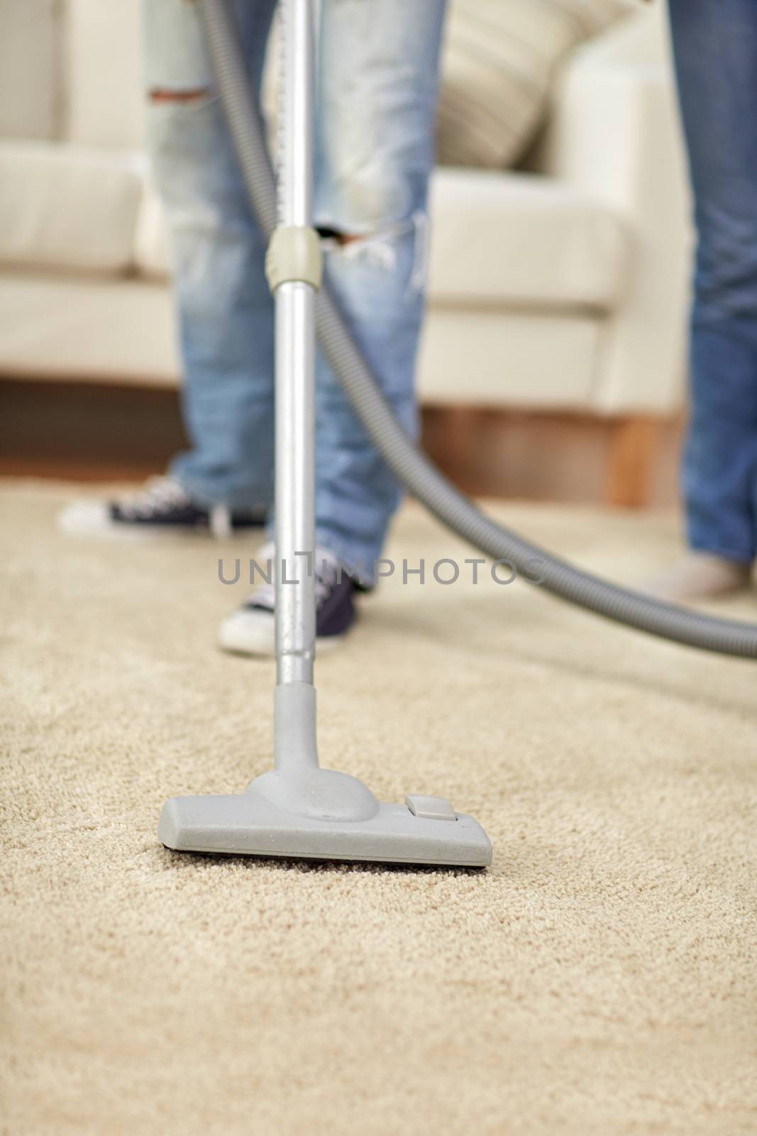 people, housework and housekeeping concept - close up of human legs and vacuum cleaner on carpet at home