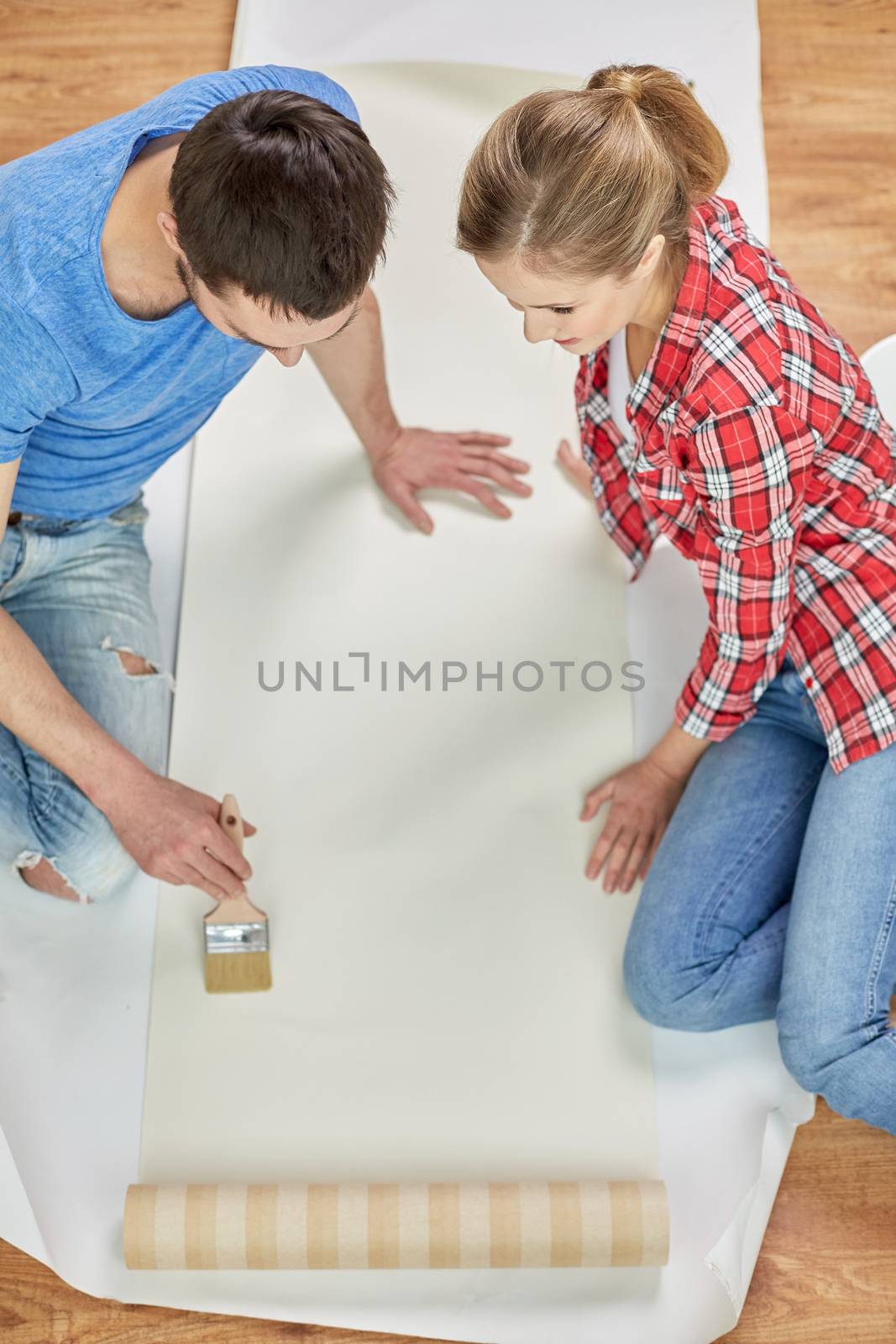 repair, renovation, building and people concept - close up of couple smearing wallpaper with glue on floor at home