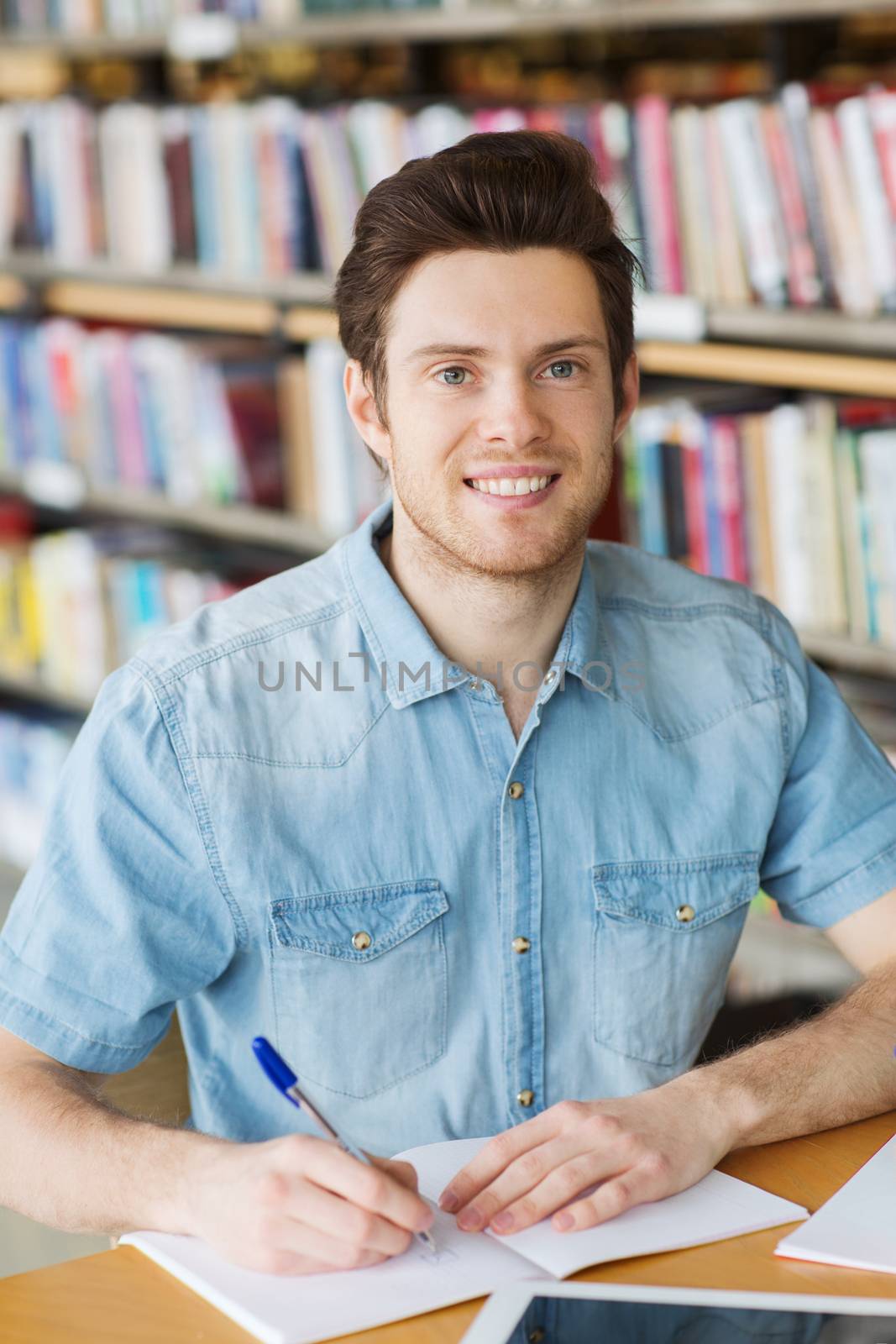 people, knowledge, education and school concept - happy student writing to notebook in library