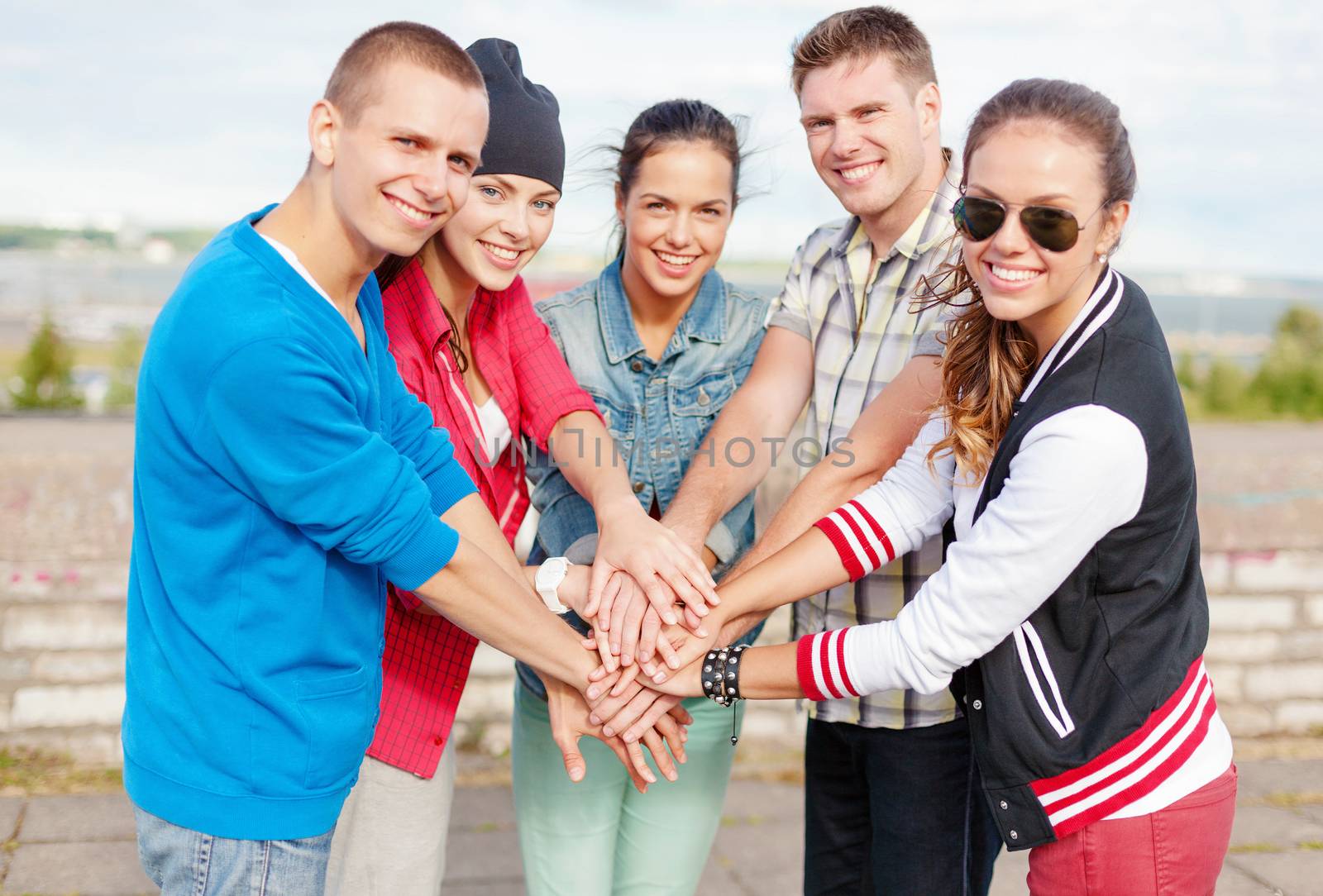 success and gesture concept - group of smiling teenagers with hands on top of each other outdoors