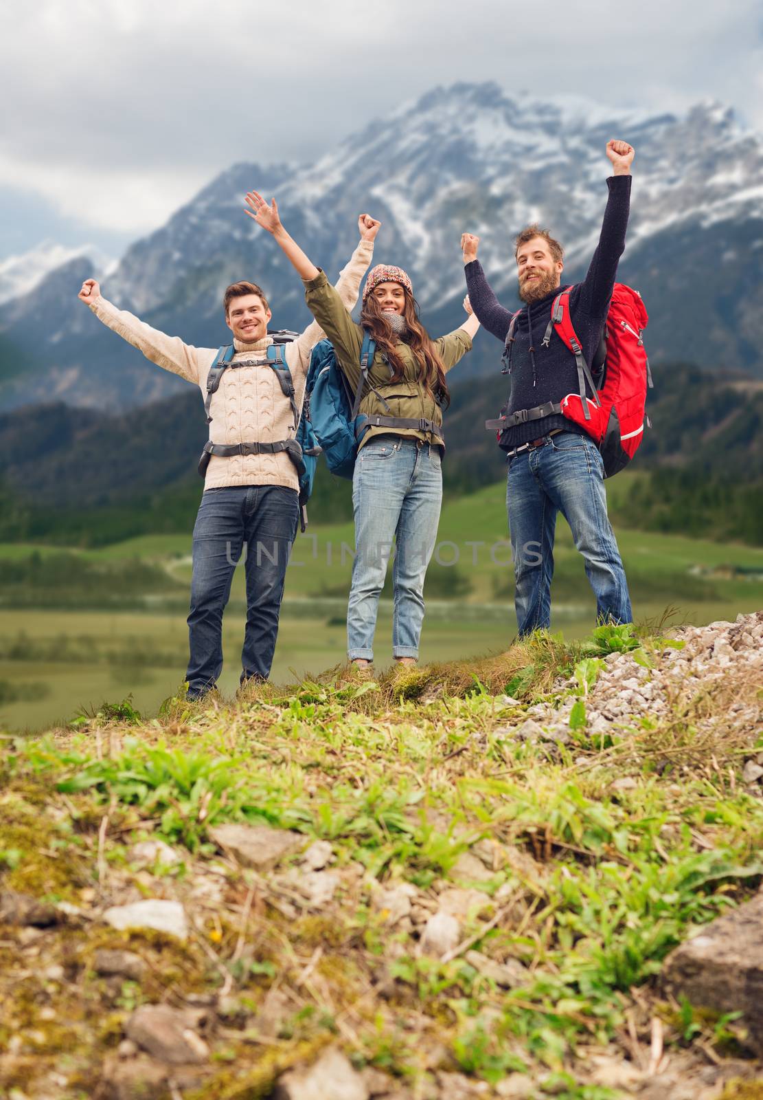 travel, tourism, hike, gesture and people concept - group of smiling friends with backpacks raising hands over mountains background