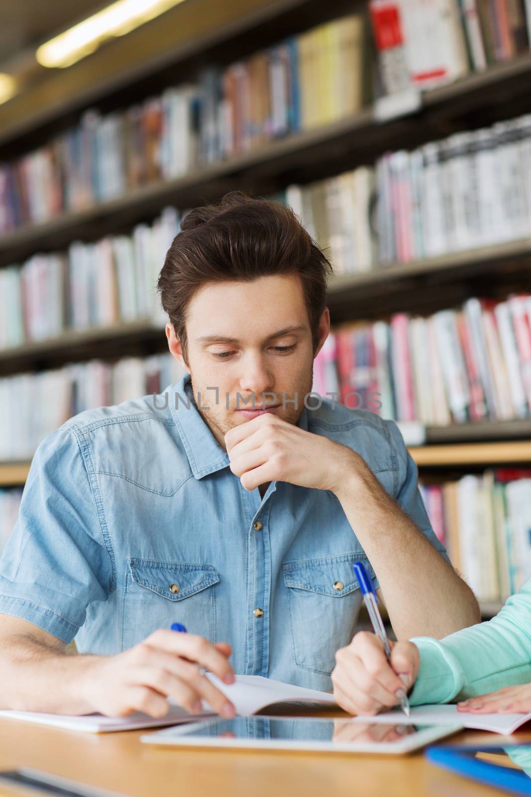 people, education, technology and school concept - male student with tablet pc computer networking in library