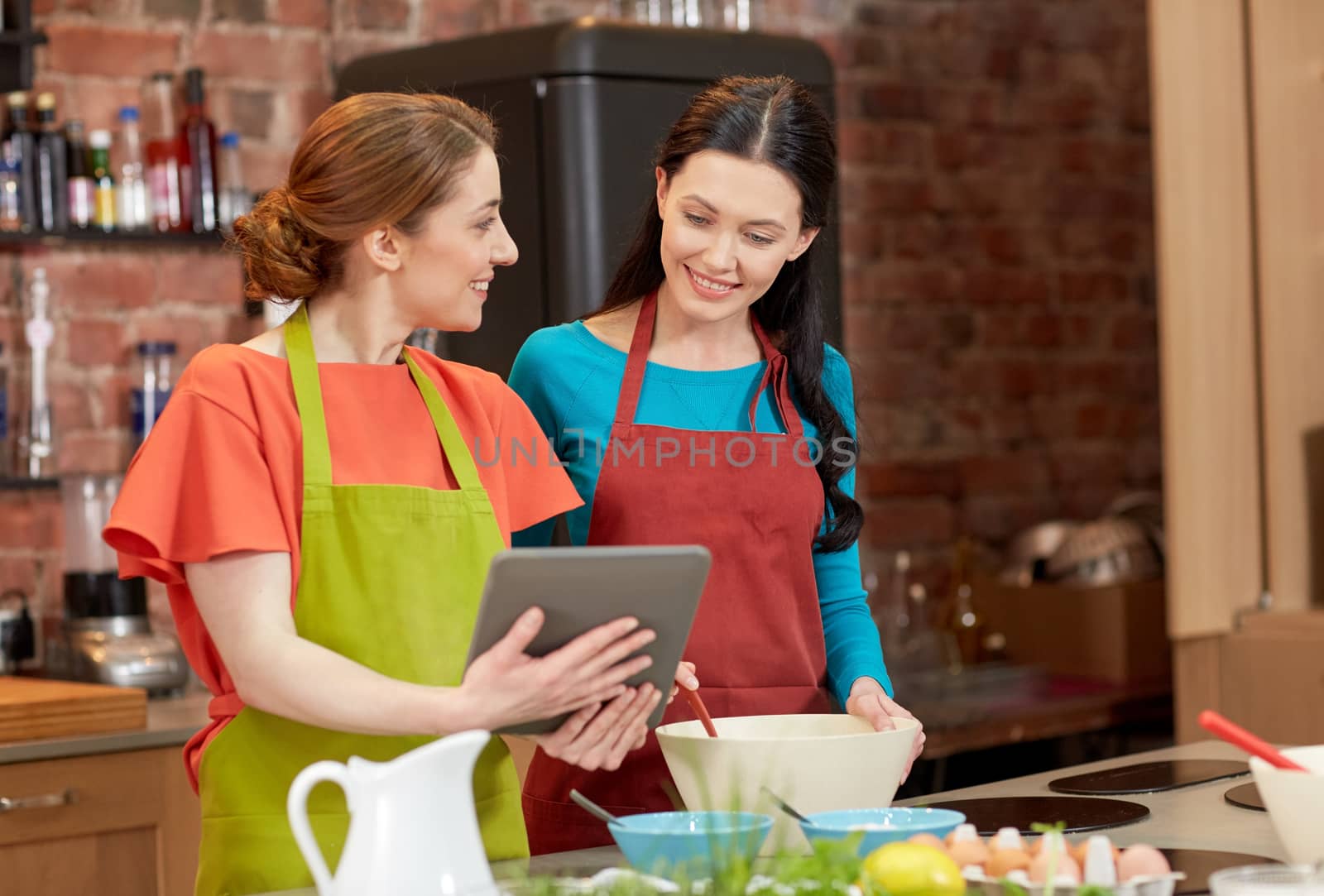 happy women with tablet pc cooking in kitchen by dolgachov