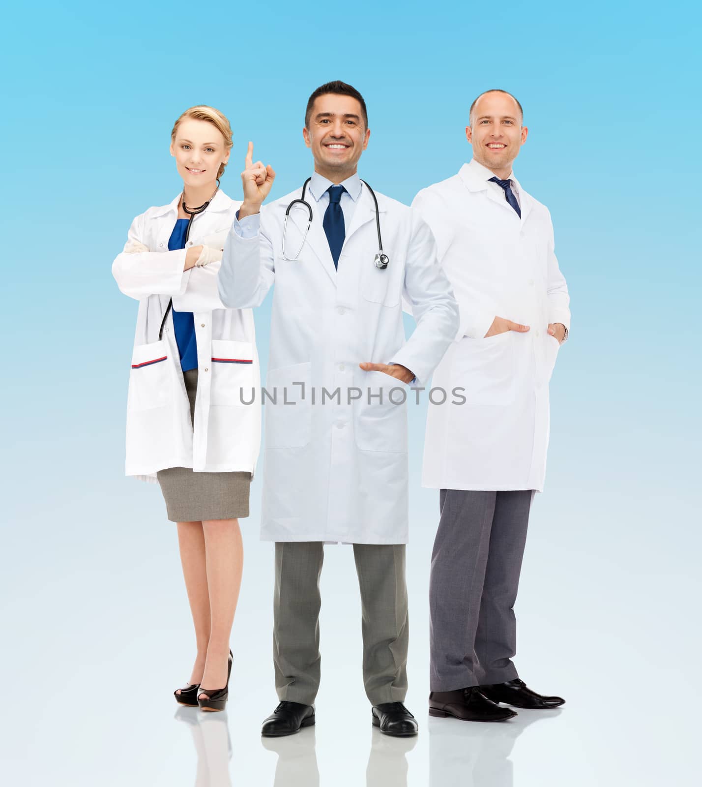 healthcare, announcement, people and medicine concept - group of smiling doctors in white coats pointing finger up and warning over blue background