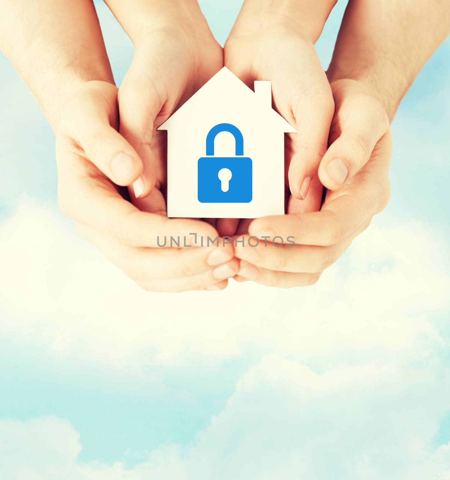 real estate and family home security concept - closeup picture of male and female hands holding white paper house with blue lock