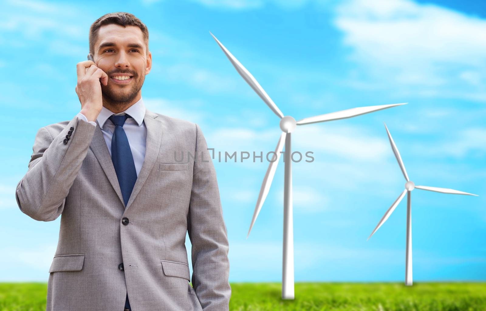 business, technology, innovation, energy saving and people concept - smiling businessman calling on smartphone over windmills and blue sky background