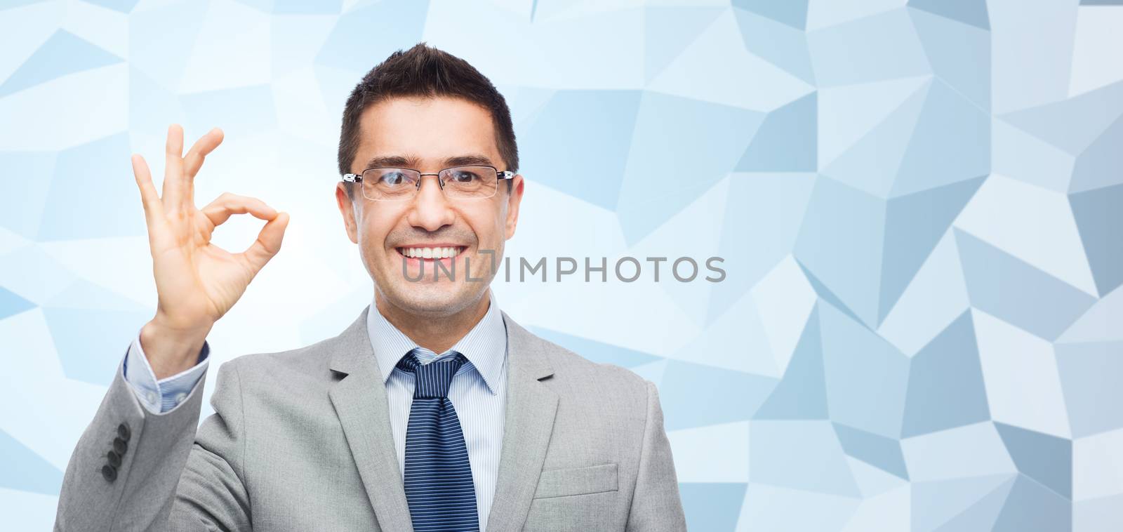 business, people, vision and office concept - happy smiling businessman in eyeglasses and suit showing ok gesture over gray graphic low poly background