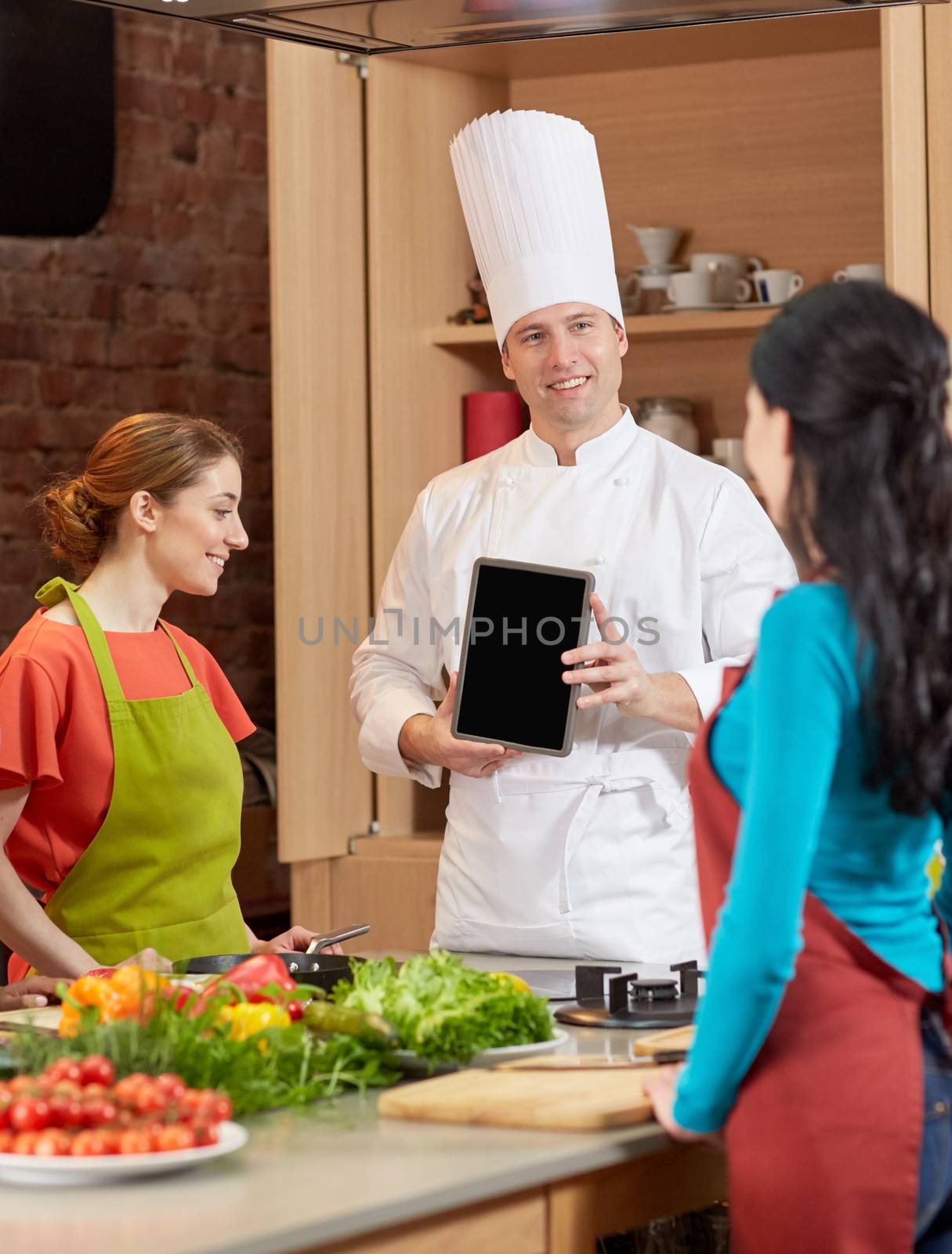 cooking class, culinary, food, technology and people concept - happy women with chef cook showing blank tablet pc screen in kitchen