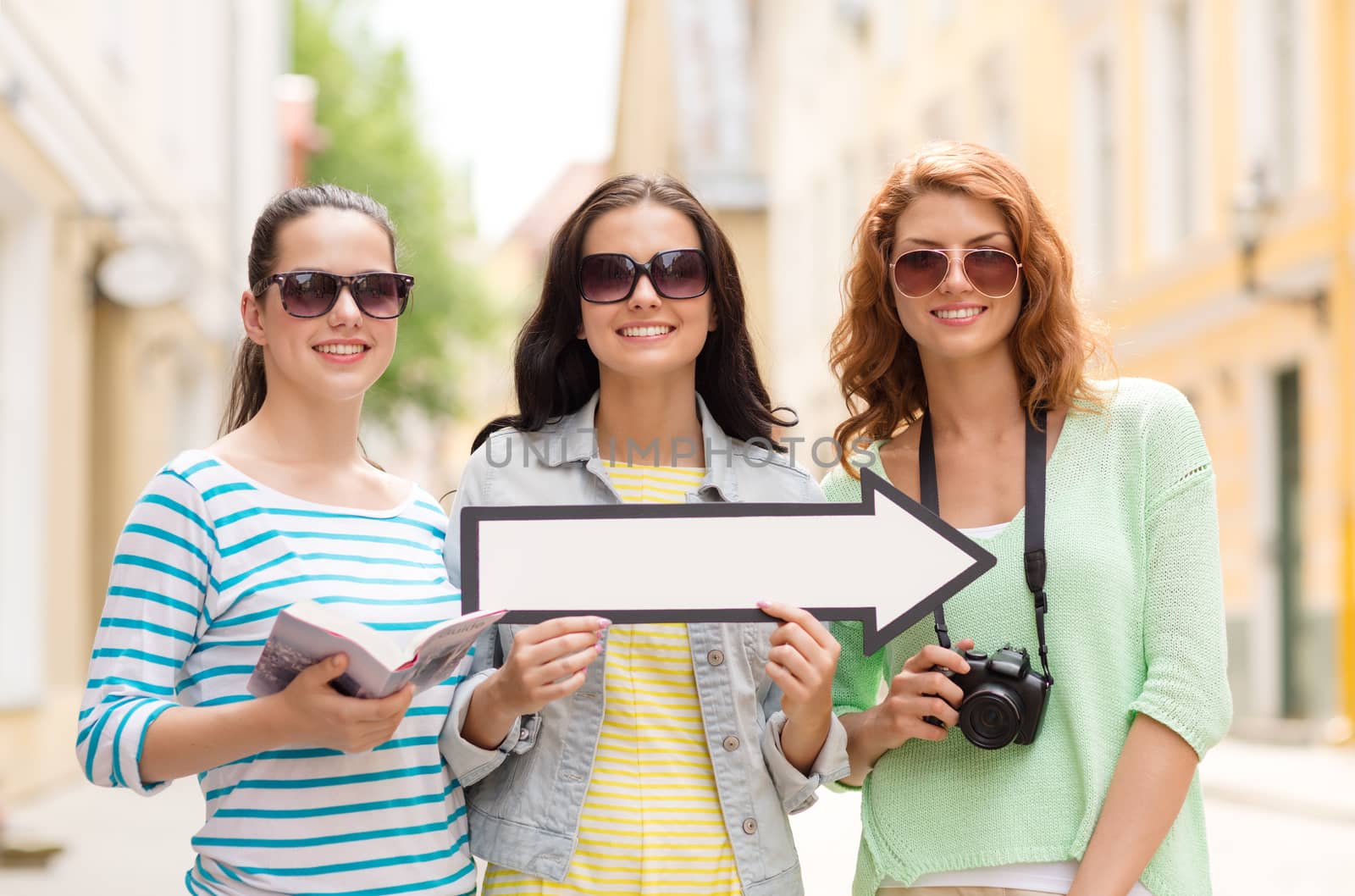 tourism, travel, vacation, direction and friendship concept - smiling teenage girls with white arrow showing direction outdoors
