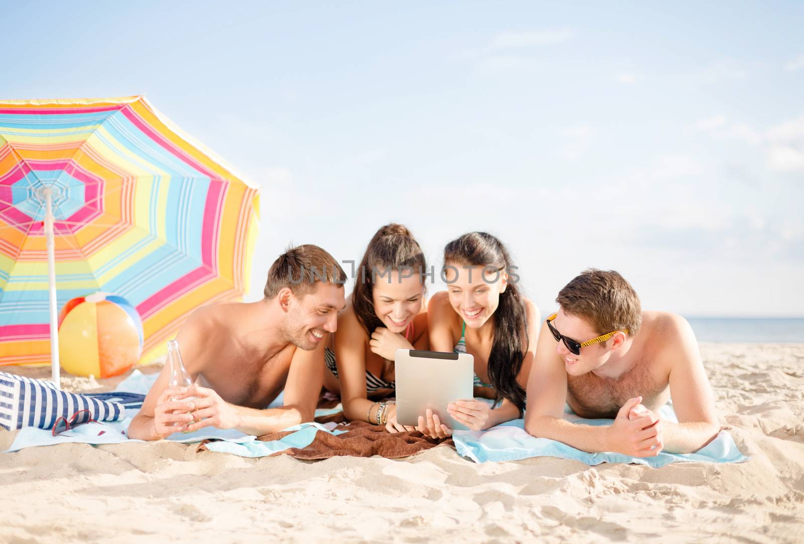 summer holidays, vacation, technology and people concept - group of happy friends with tablet pc computer sunbathing on beach