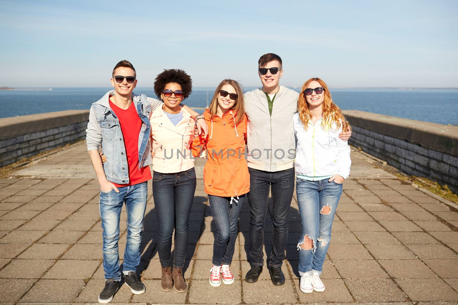 tourism, travel, people and leisure concept - group of happy teenage friends in sunglasses hugging on city street