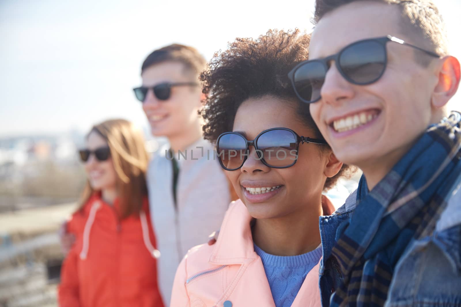 happy teenage friends in shades hugging on street by dolgachov