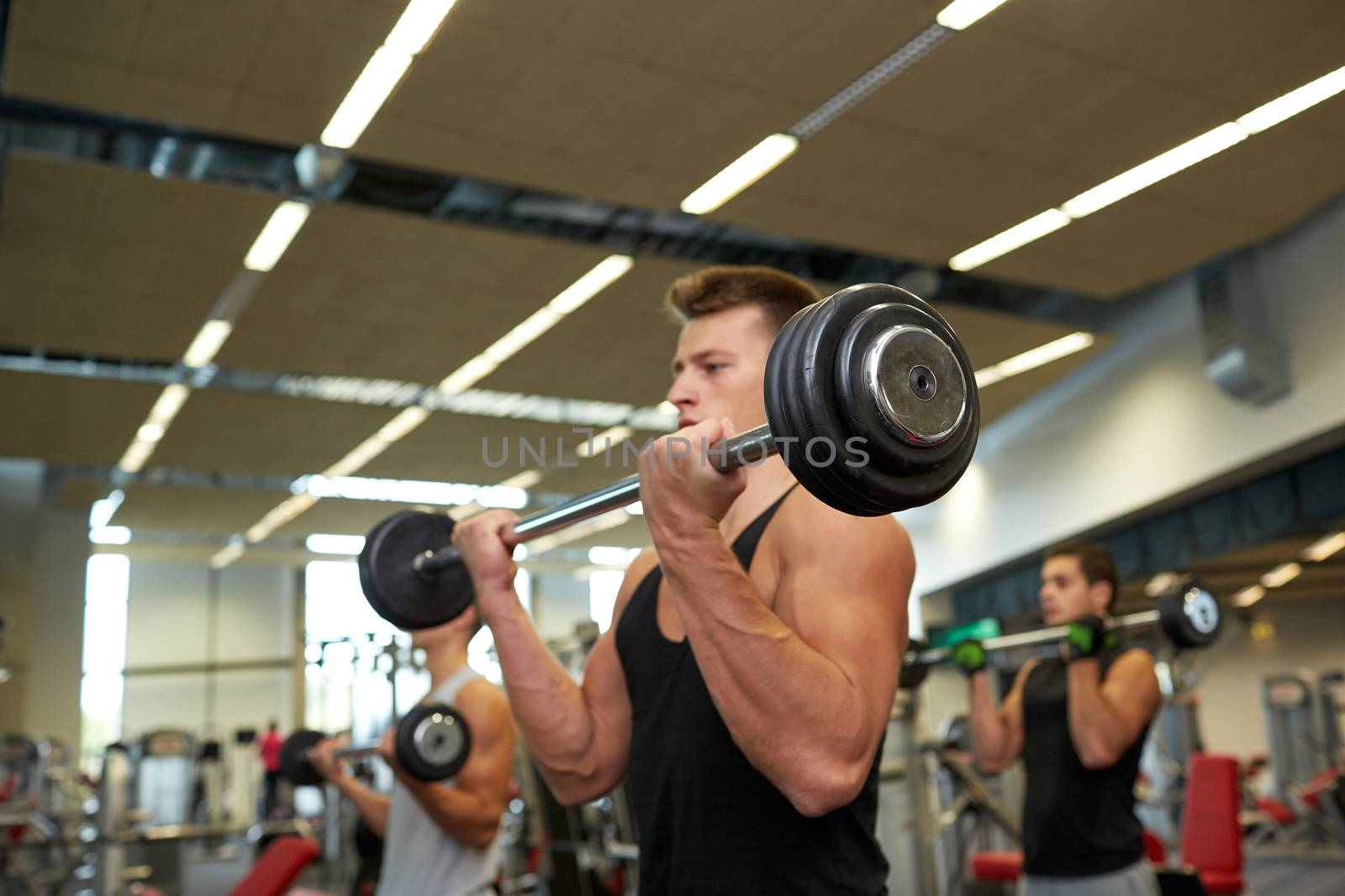 young men flexing muscles with barbells in gym by dolgachov