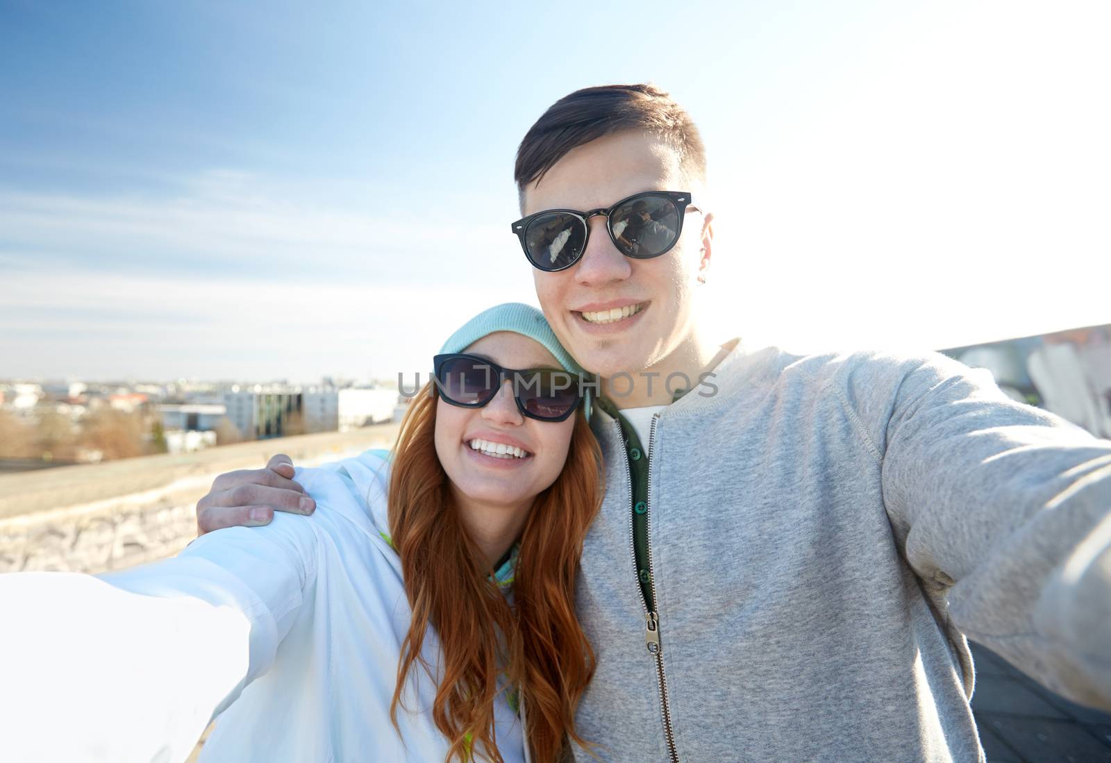 happy teenage couple taking selfie on city street by dolgachov