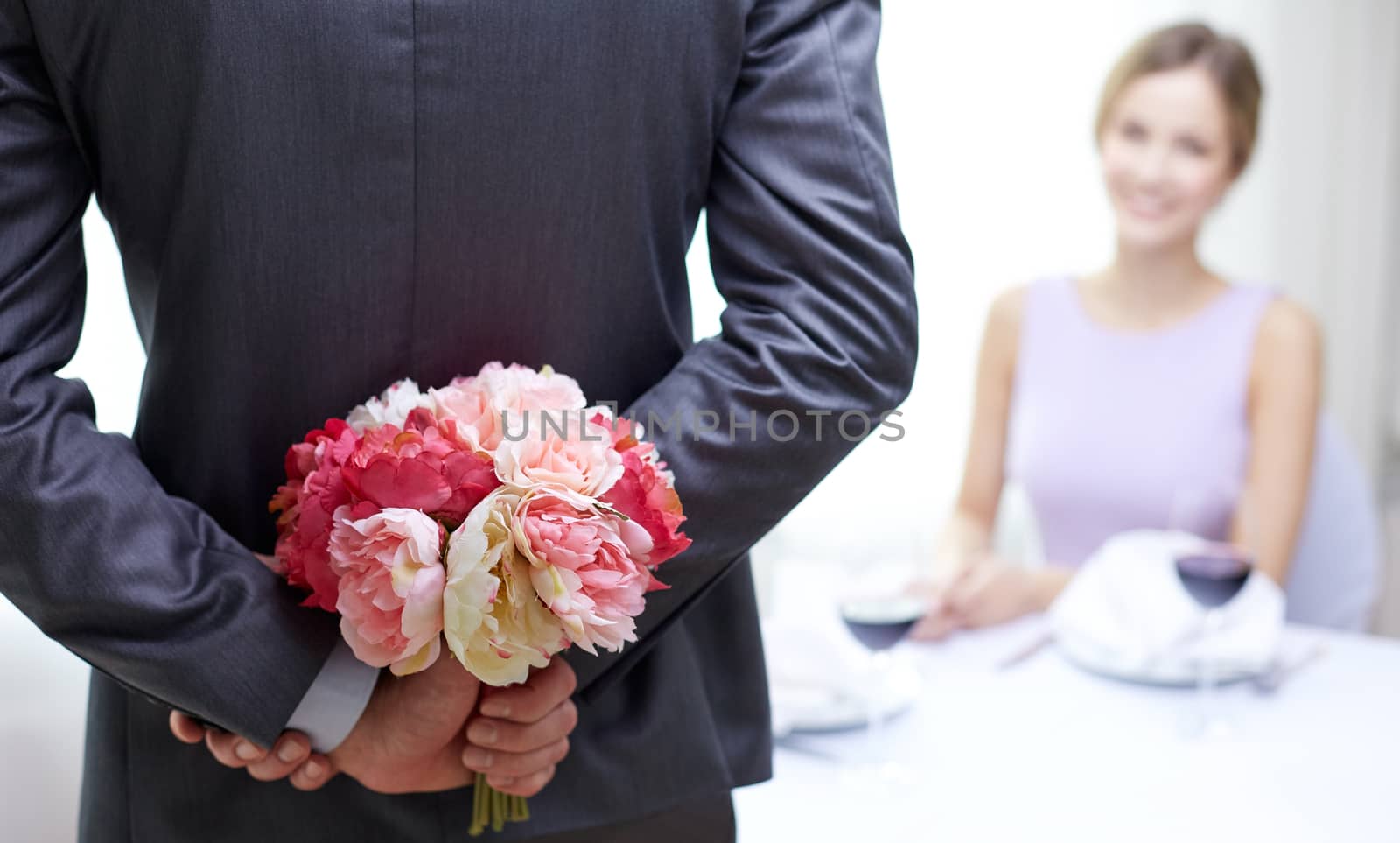 restaurant, people, celebration and holiday concept - close up of man hiding flowers behind from woman at restaurant