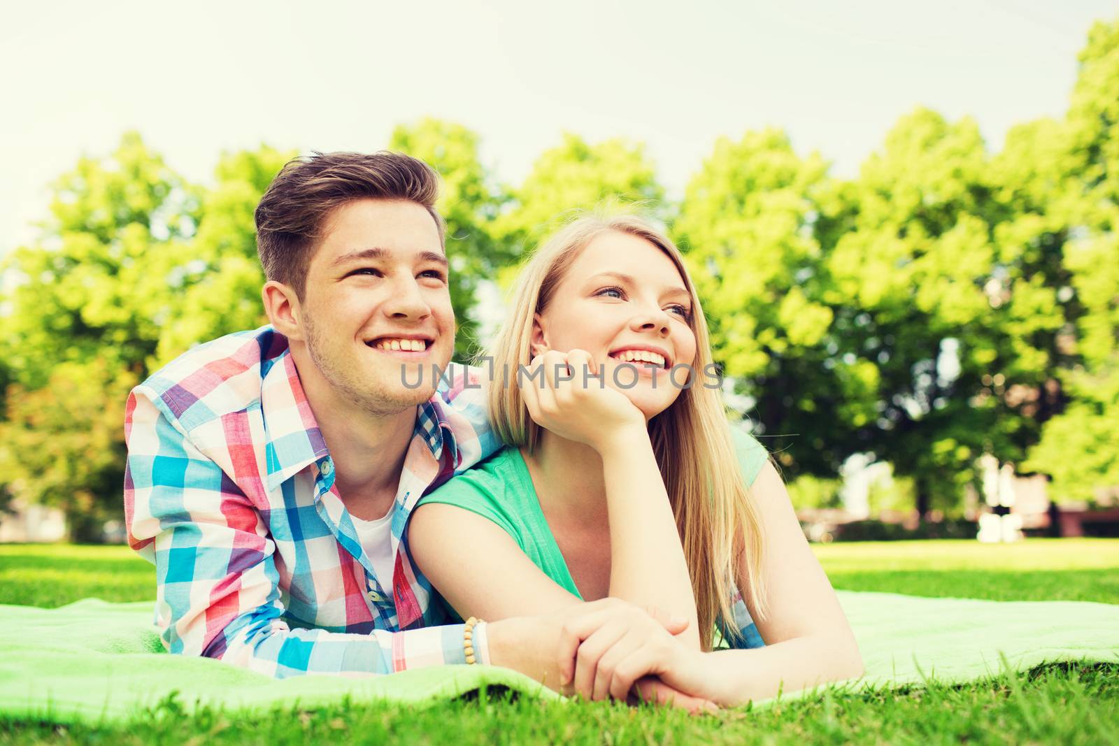 holidays, vacation, love and friendship concept - smiling couple lying on blanket in park