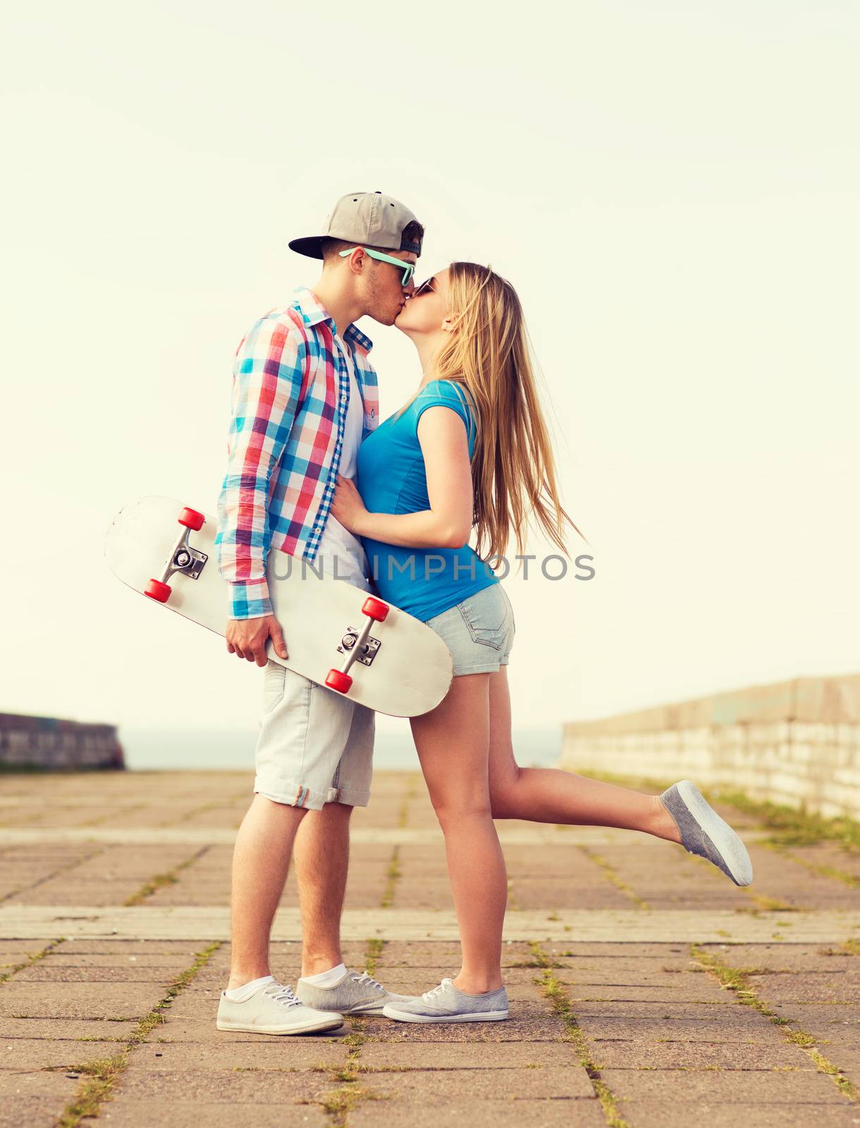 smiling couple with skateboard kissing outdoors by dolgachov