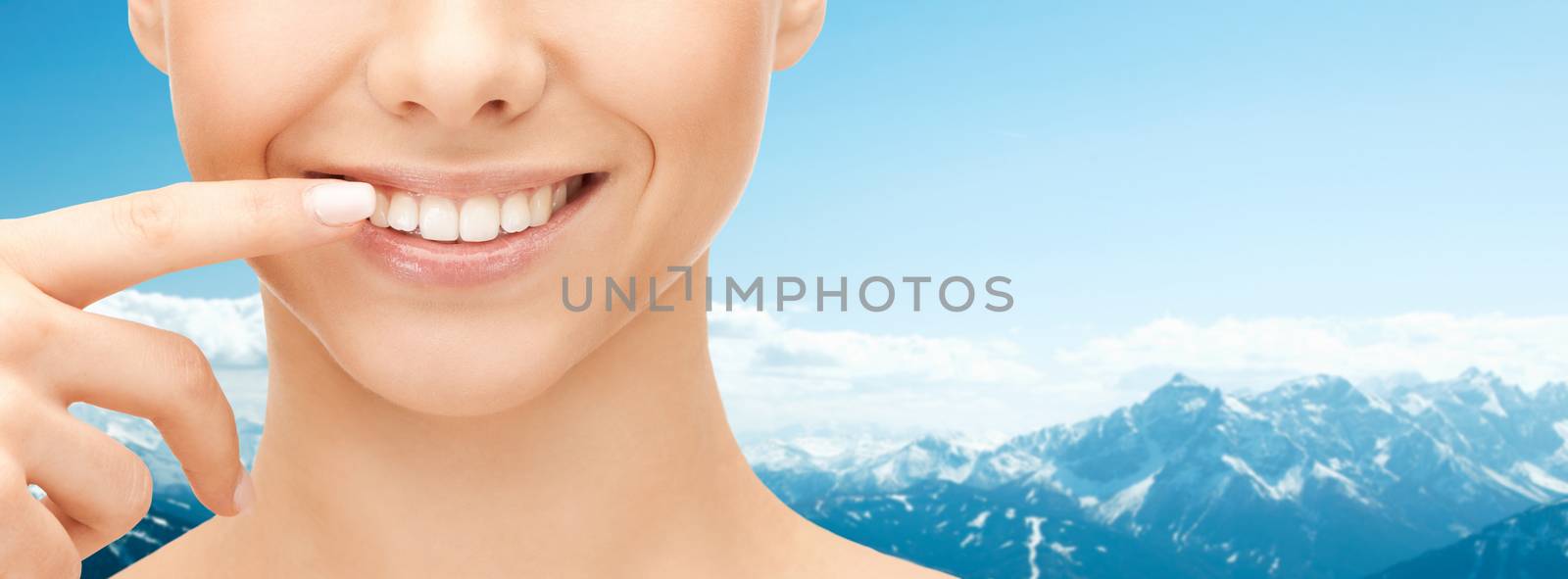 dental health, beauty, hygiene and people concept - close up of smiling woman face pointing to teeth over blue mountains background