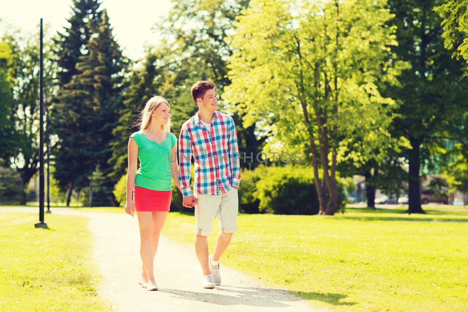 holidays, vacation, love and friendship concept - smiling couple walking and holding hands in park