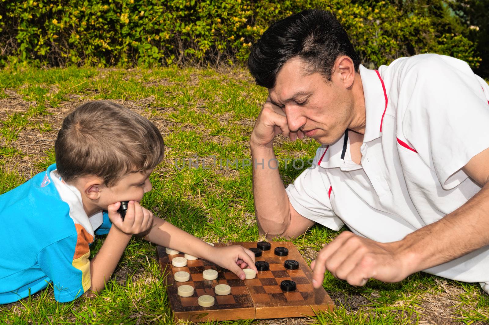 Father and son playing checkers on the grass in a city park