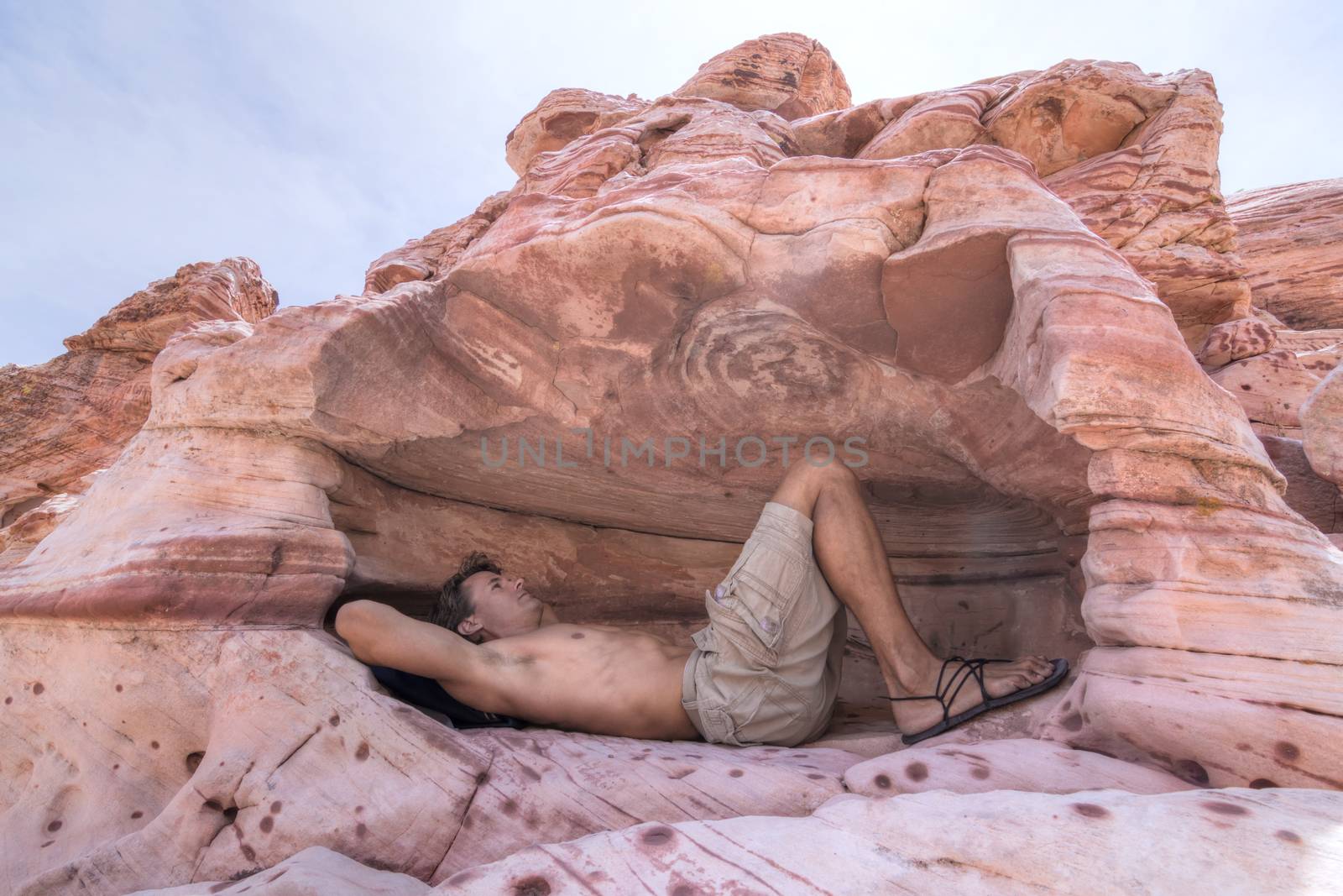 Caucasian male hiker takes refuge from hot desert sun in a shallow cave in Red Rock Canyon, Las Vegas