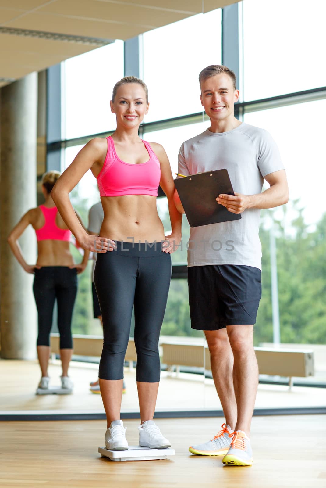 sport, fitness, lifestyle and people concept - smiling man and woman with scales and clipboard in gym