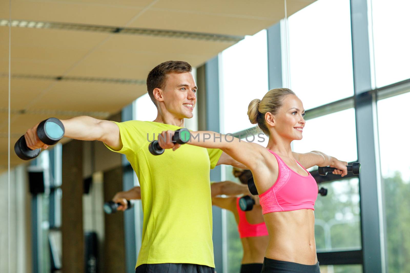 smiling man and woman with dumbbells in gym by dolgachov