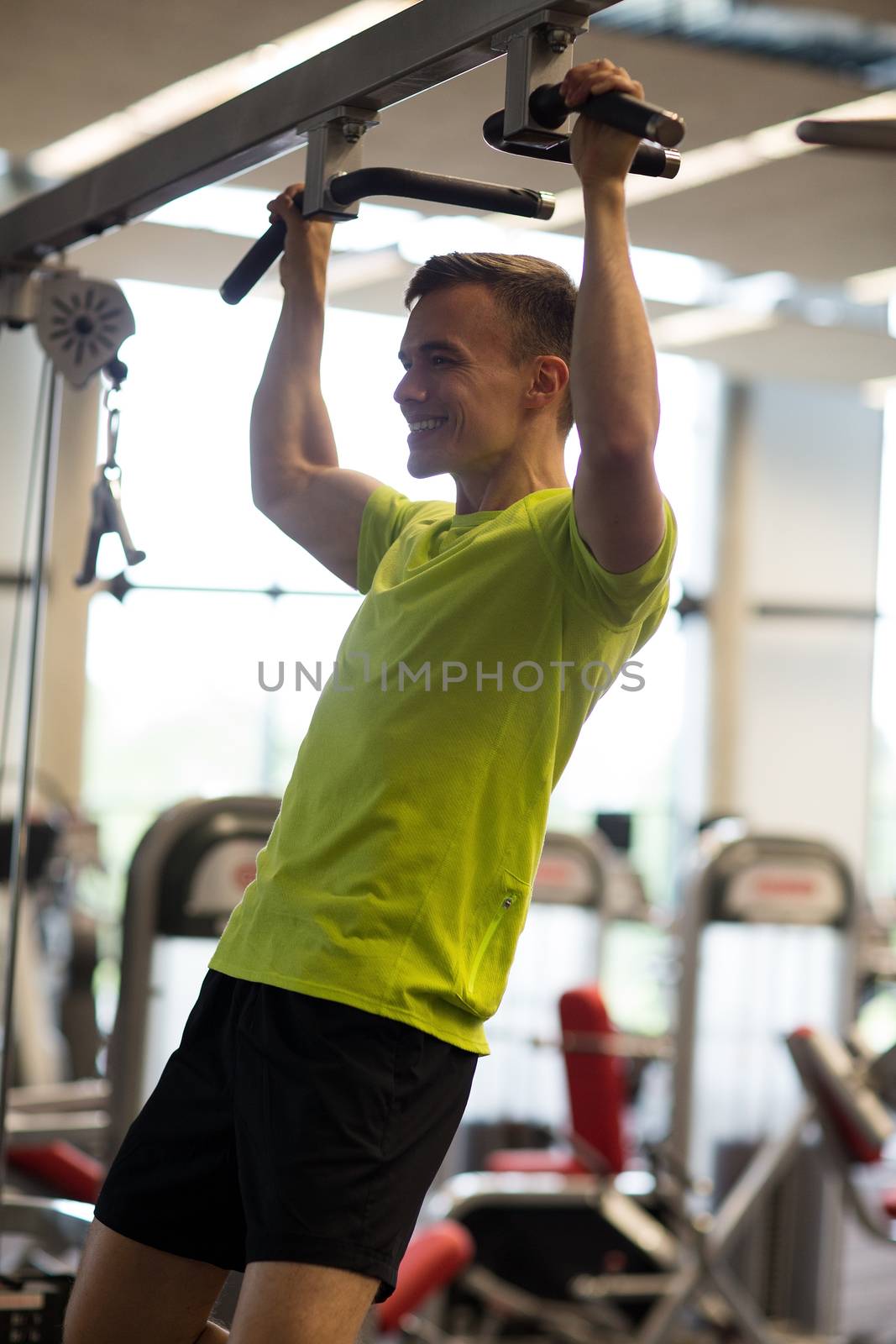 sport, fitness, lifestyle and people concept - smiling man doing pull-ups in gym