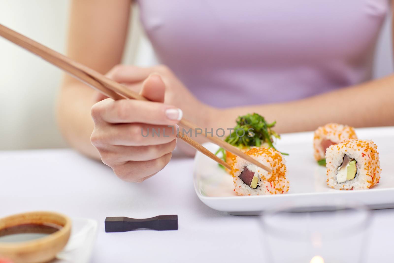 restaurant, food, people, asian and japanese kitchen concept - close up of woman eating sush with chopsticks at restaurant